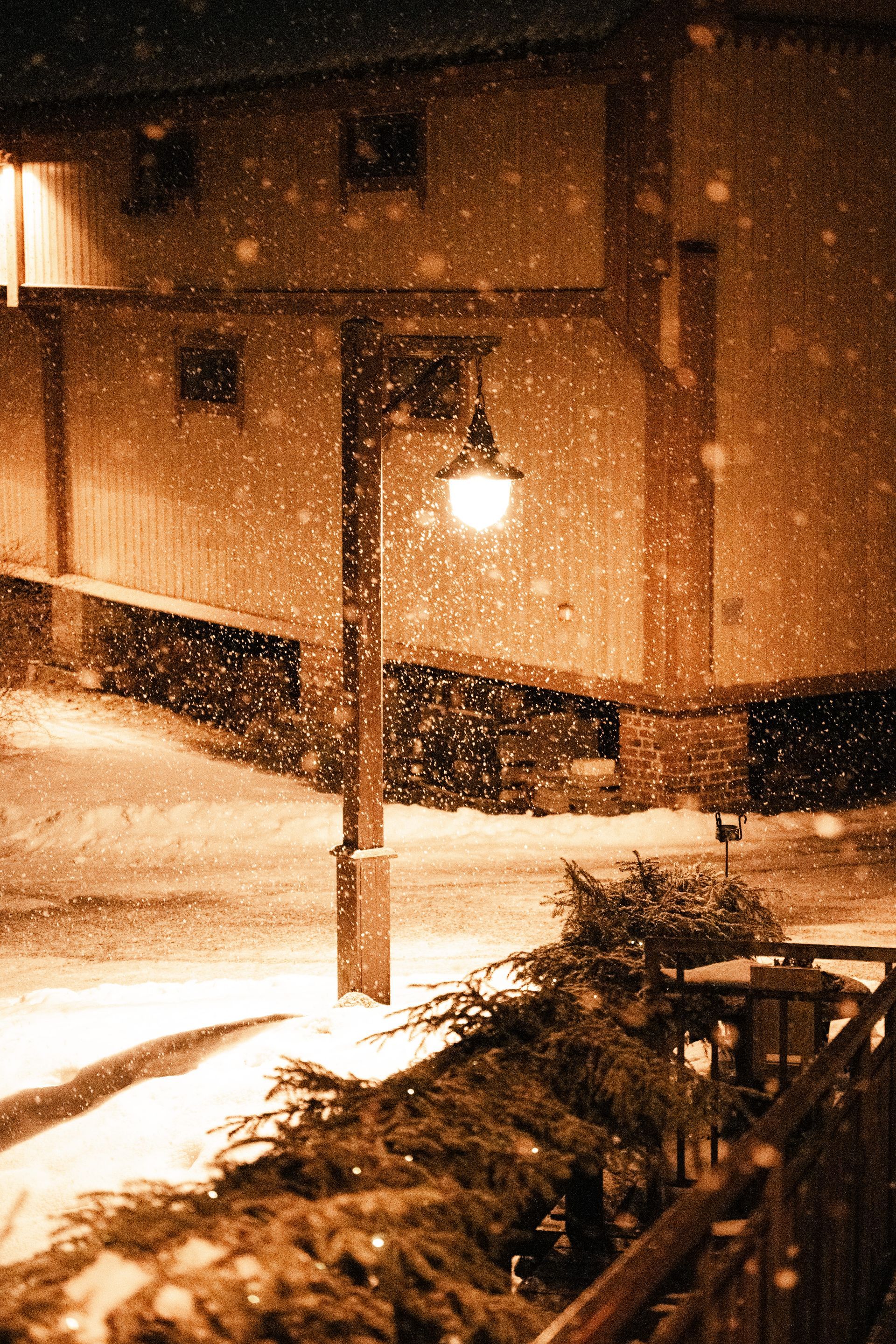 Snødekt gate om natten med en tent lyktestolpe ved siden av en bygning og fallende snø.