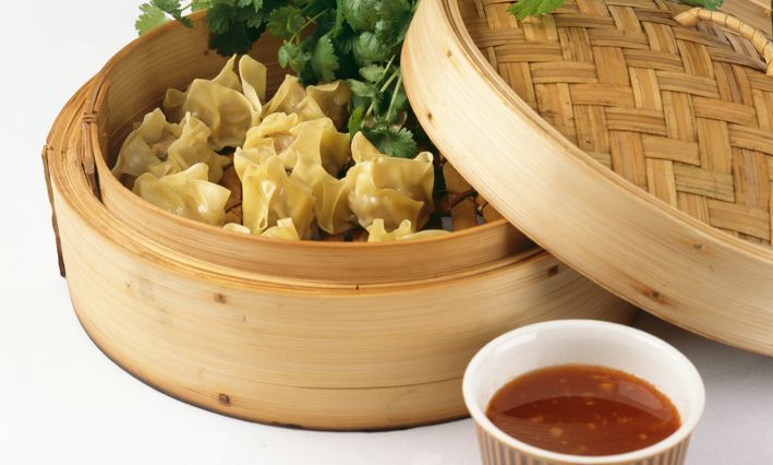 Dampede dumplings servert i en bambuskurv med dippsaus og koriander ved siden av.