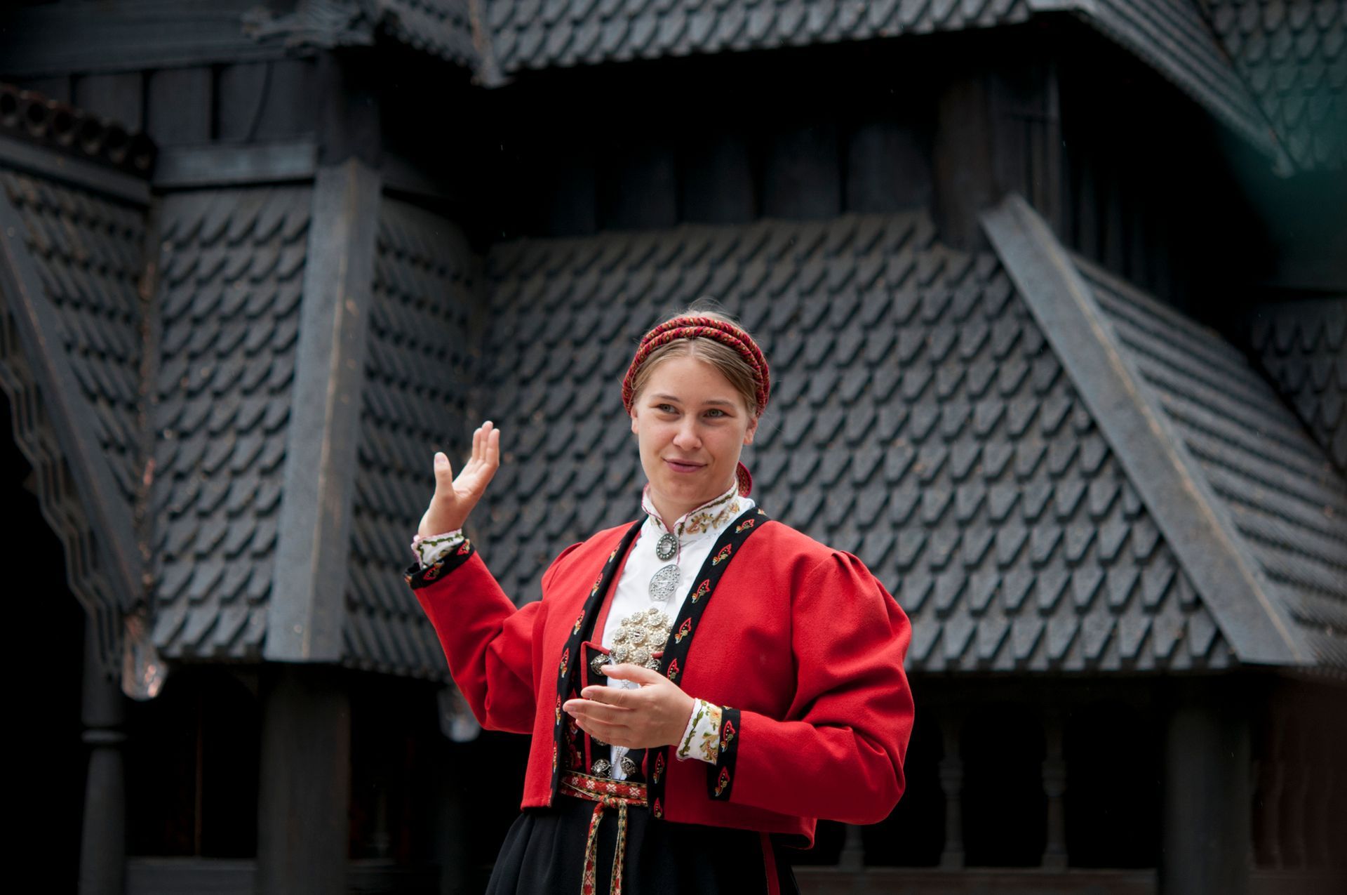 Omviser i bunad står foran Stavkirken på Norsk Folkemuseum.