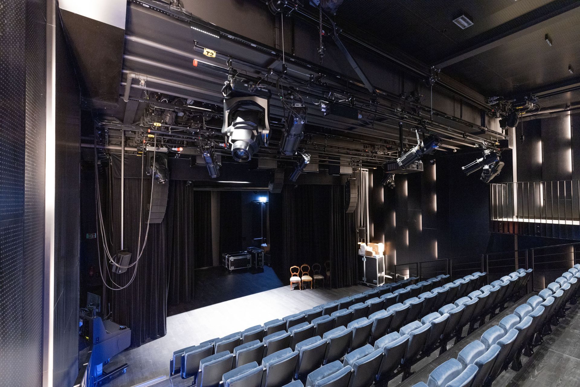 Et vidvinkelbilde av et mørkt teater med rader med tomme blå seter vendt mot en scene opplyst av spotlights over hodet.