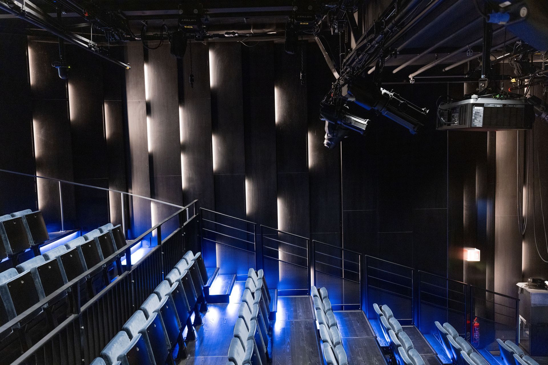 Et tomt teater med rader med seter vendt mot et sceneområde opplyst av vertikale hvite lyspaneler mot svarte vegger.