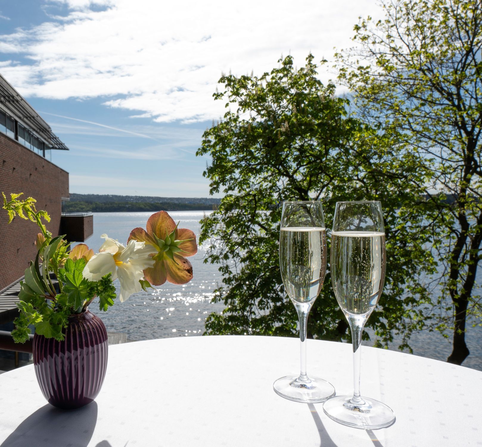To glass champagne og en liten vase med blomster og fjordutsikt