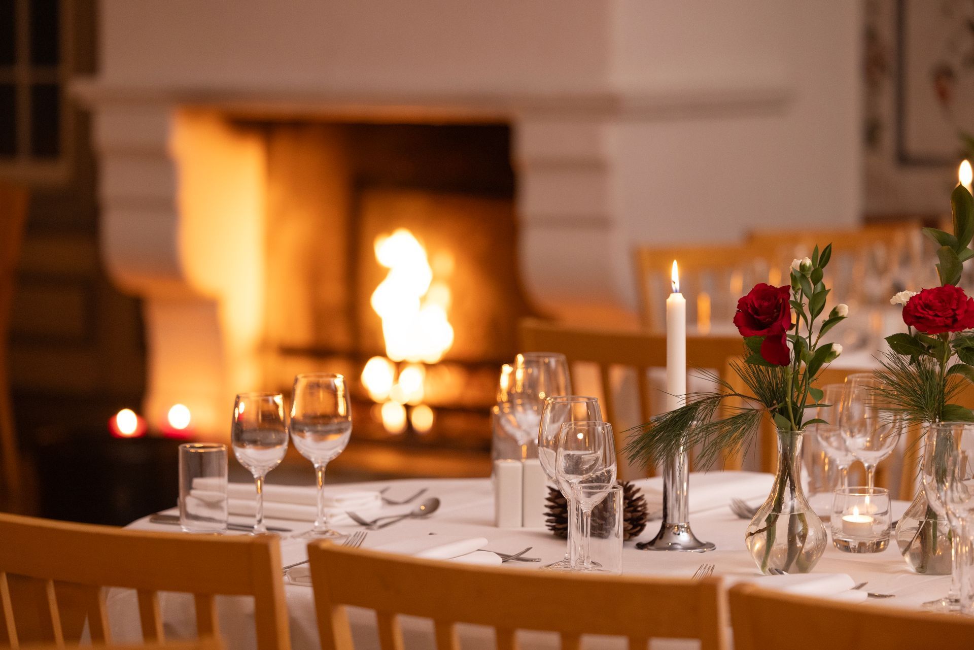 Elegant spisebord med levende lys, vinglass, blomster og en peis i bakgrunnen