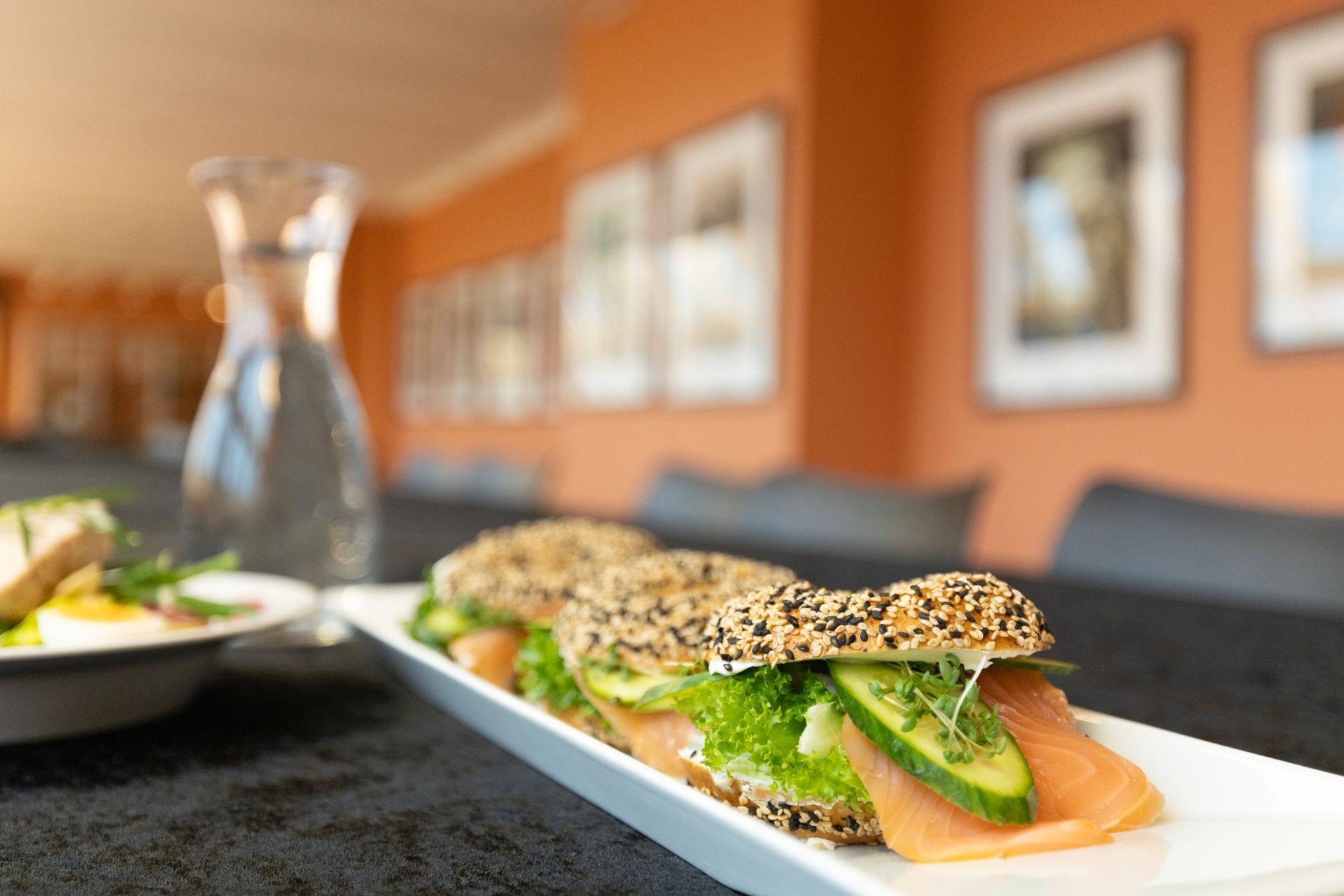Nærbilde av sandwich med laks og avokado på en hvit tallerken i en varm restaurantsetting