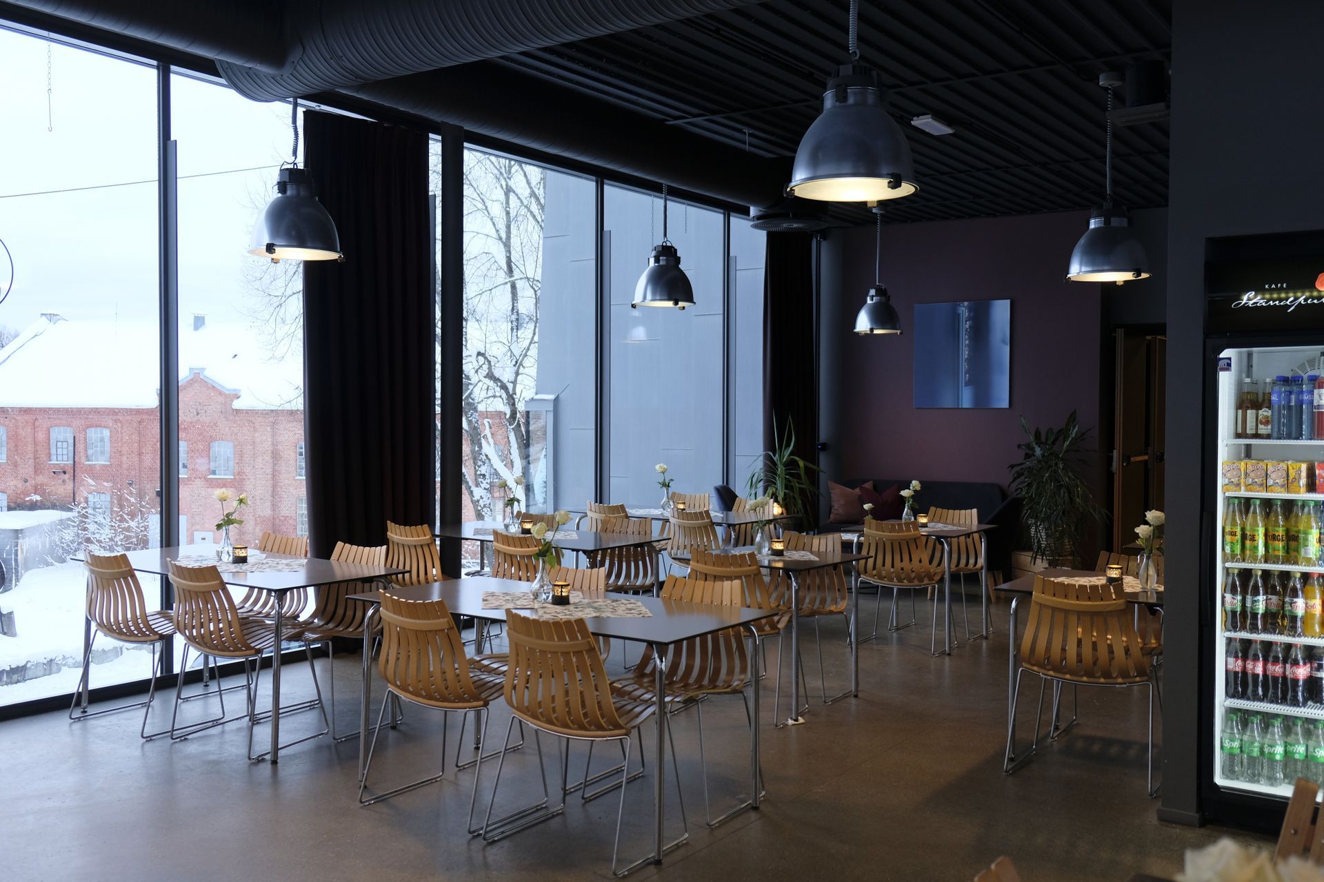 Moderne kaféinteriør med trestoler, bord, pendellamper og store vinduer som viser snødekt utendørslandskap