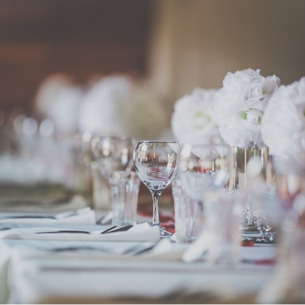 Elegant dekket bankettbord med hvite blomsterdekorasjoner og glass i mykt fokus
