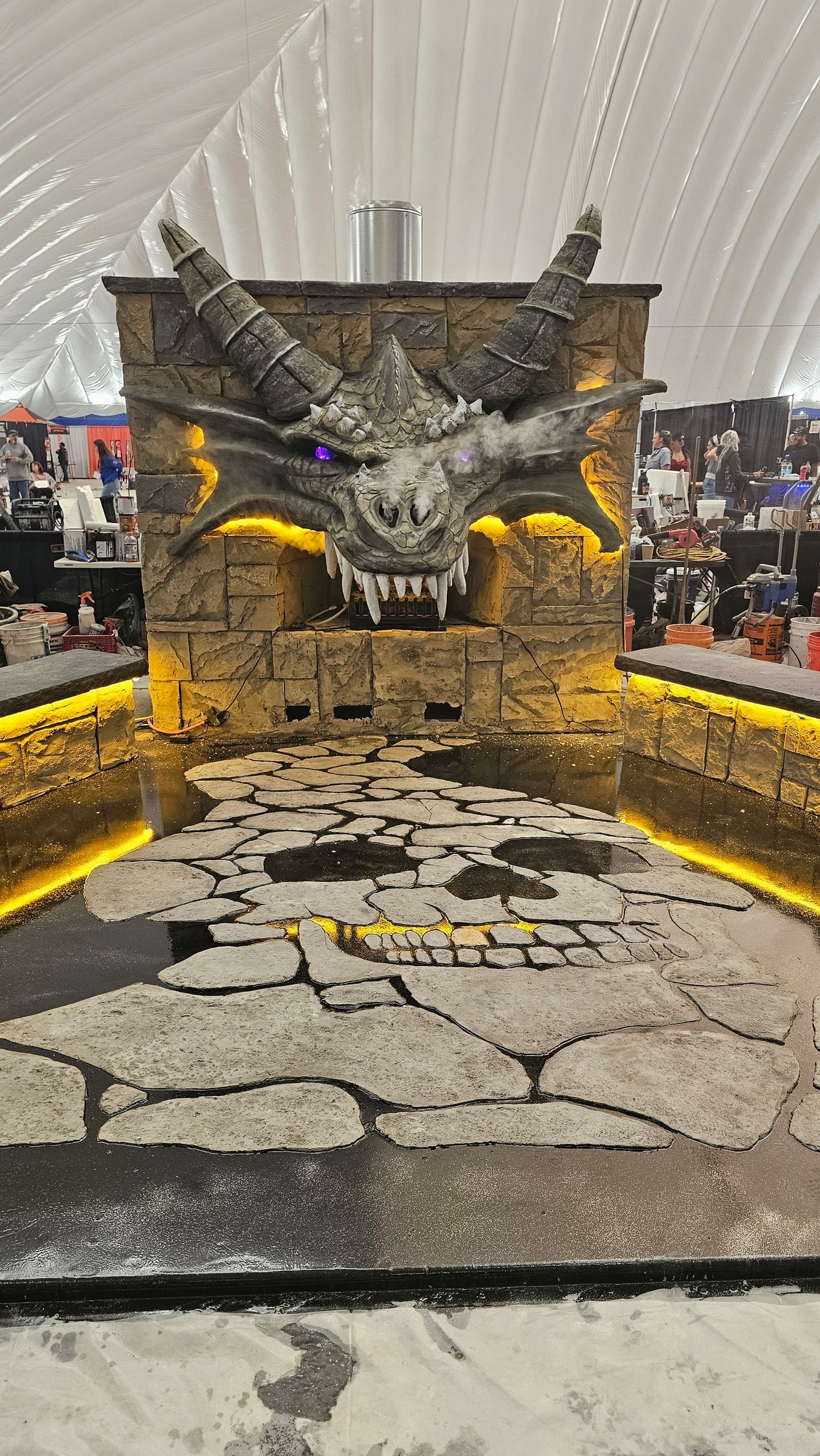 A large dragon head sculpture mounted on a stone wall above a lit, stone-tiled floor inside a high-ceilinged venue.