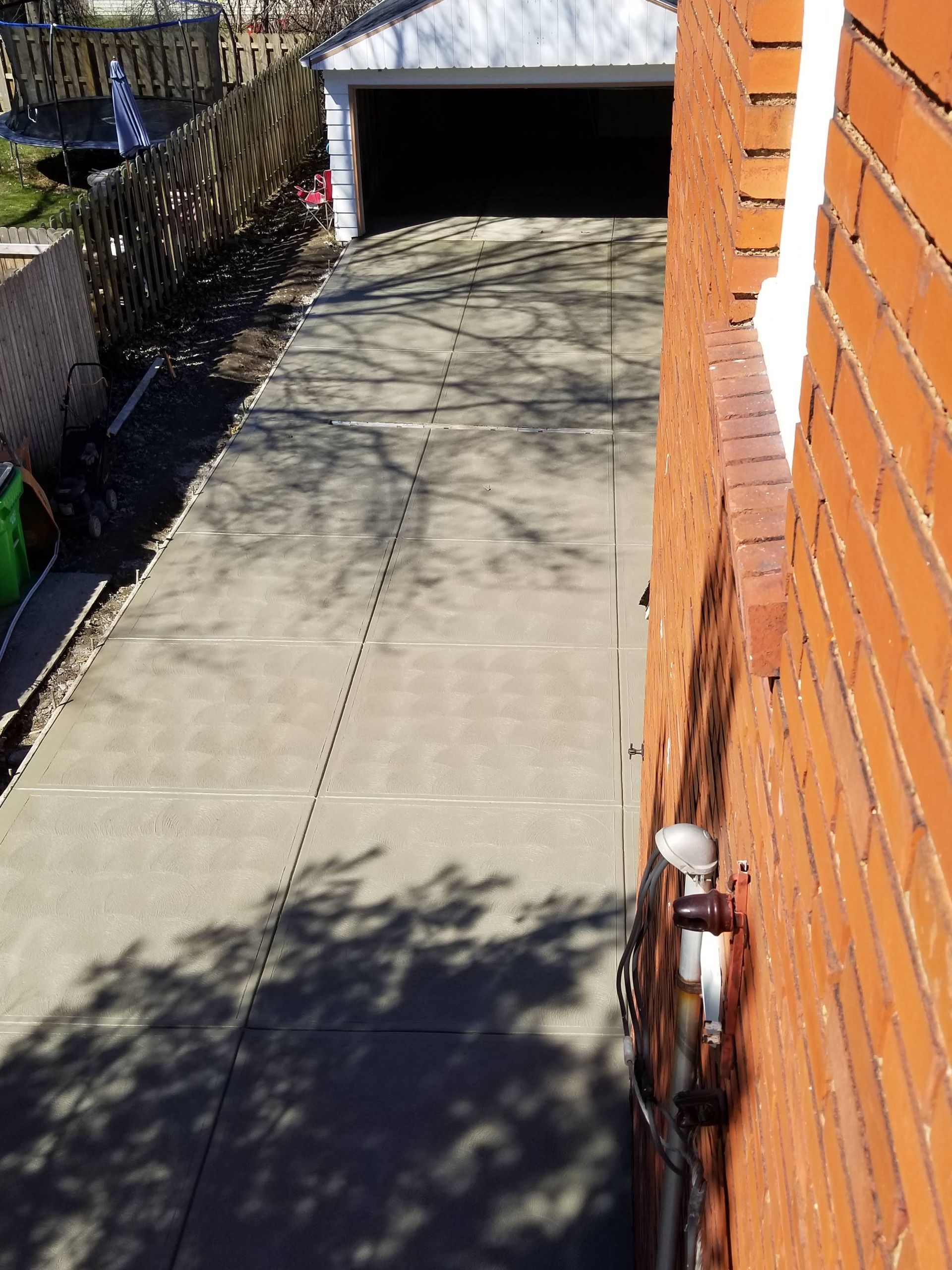 A concrete driveway leads to a detached garage alongside a red brick house wall.
