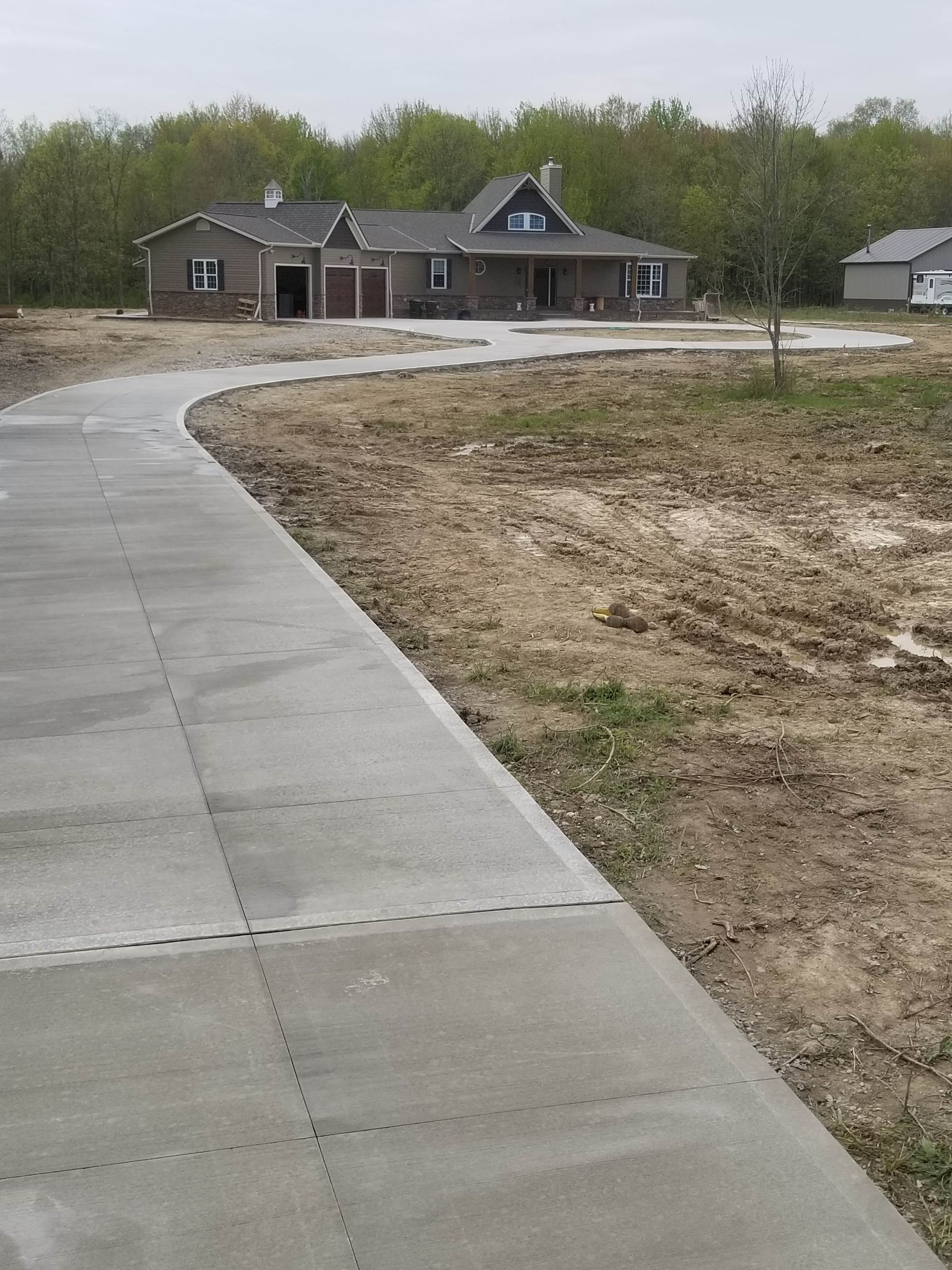 A newly paved, winding concrete driveway leading to a house surrounded by trees and unfinished landscaping.