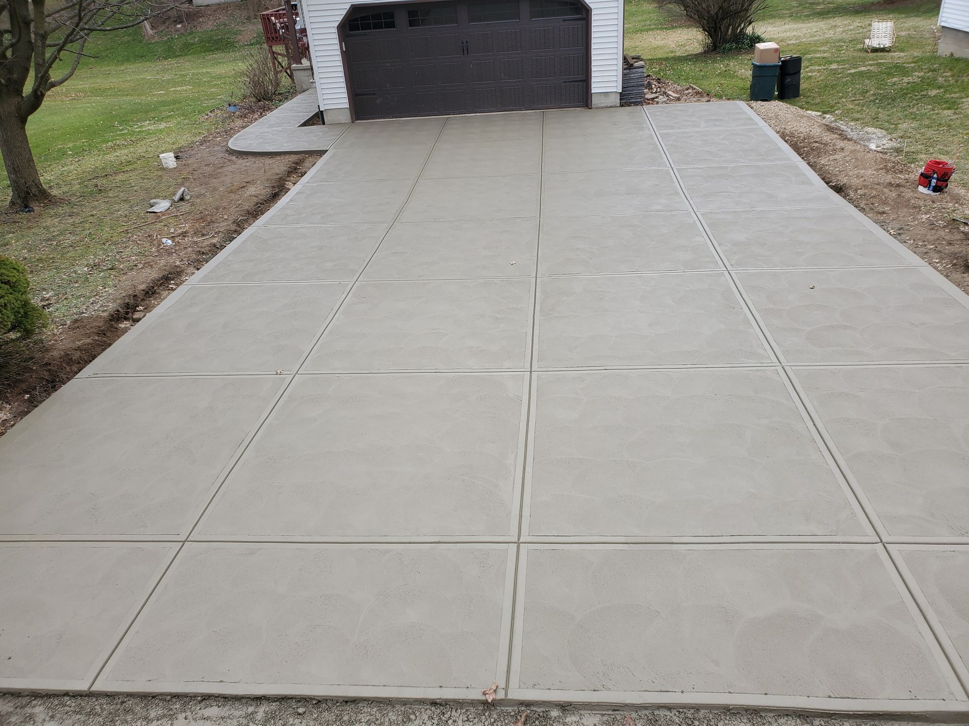 A newly poured concrete driveway with a grid of control joints leading to a garage.