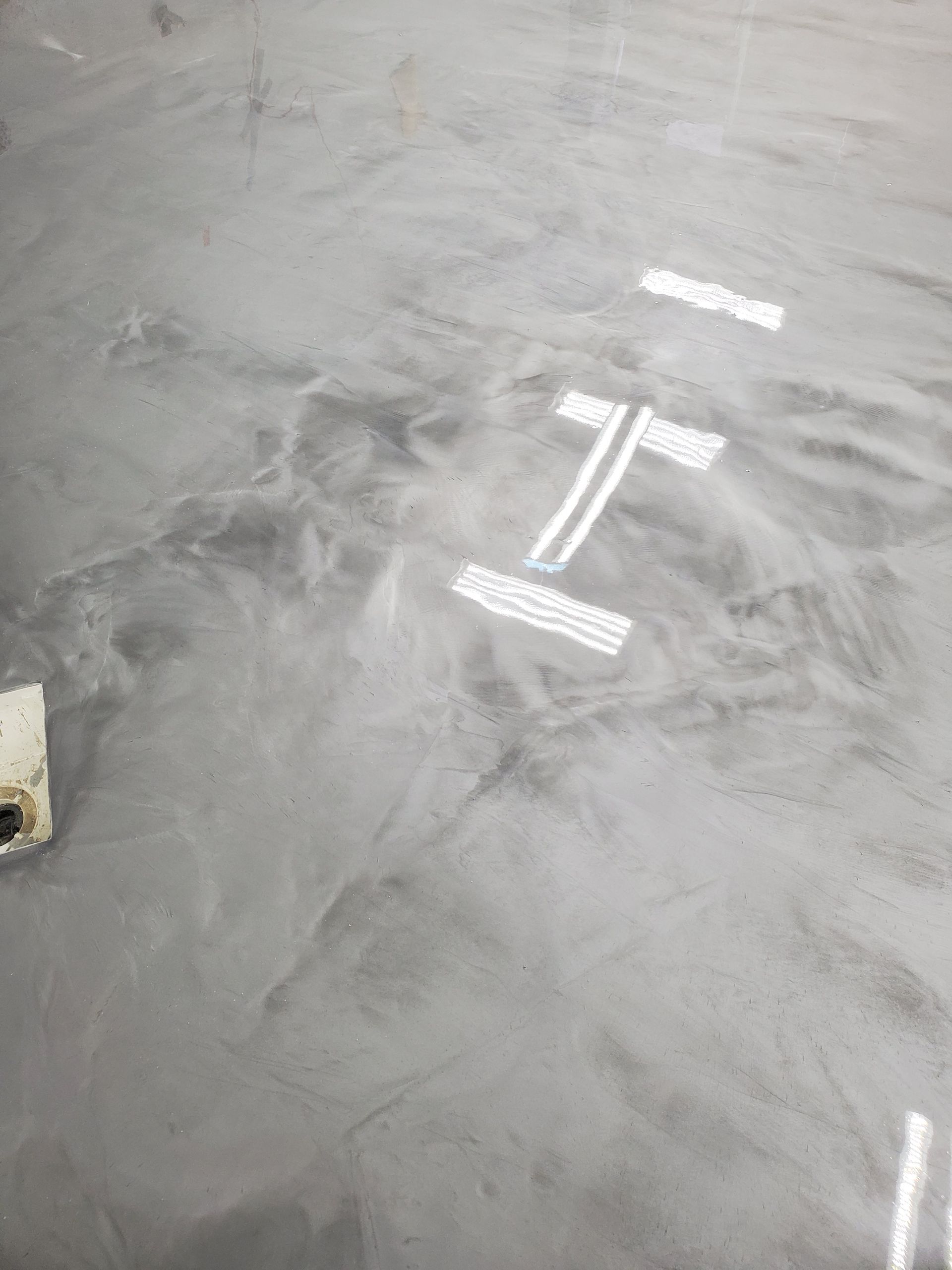 A high-gloss gray epoxy floor with subtle, marbled texture and white tape markings in the center.