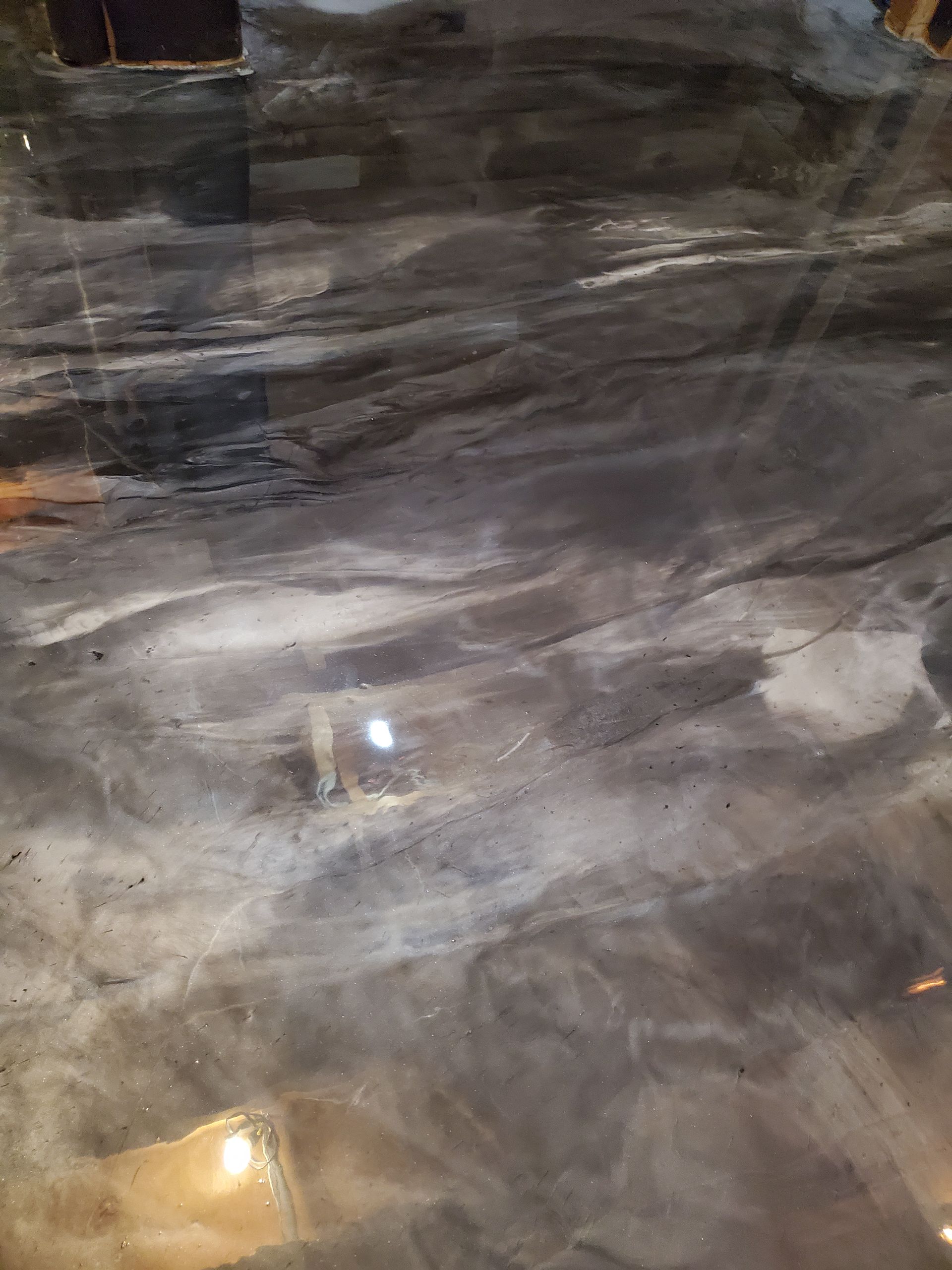 A glossy, dark grey epoxy floor surface with swirling, marble-like patterns and subtle light reflections.