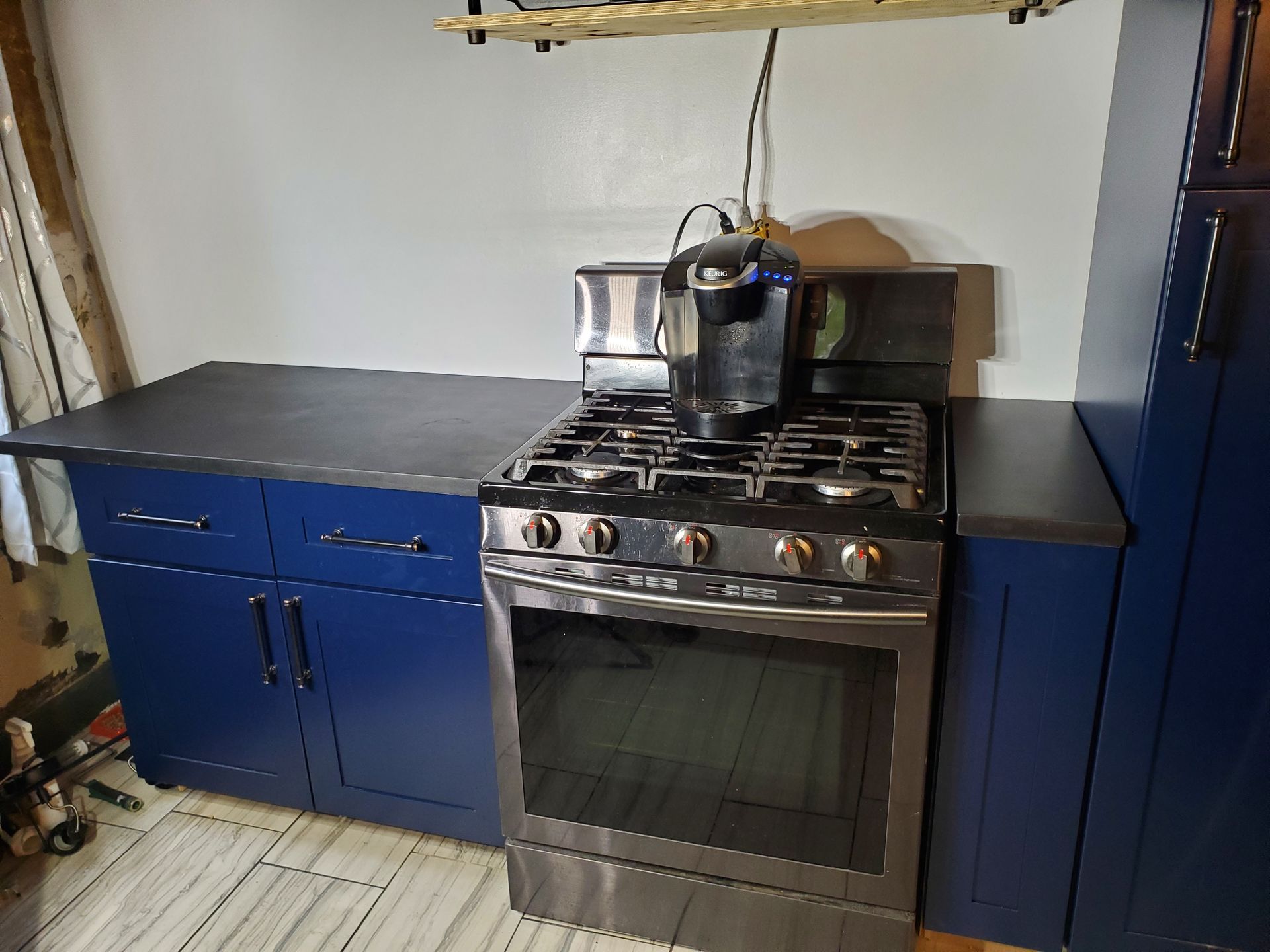A stainless steel gas stove with a coffee maker on top, situated between blue cabinets and a dark countertop.