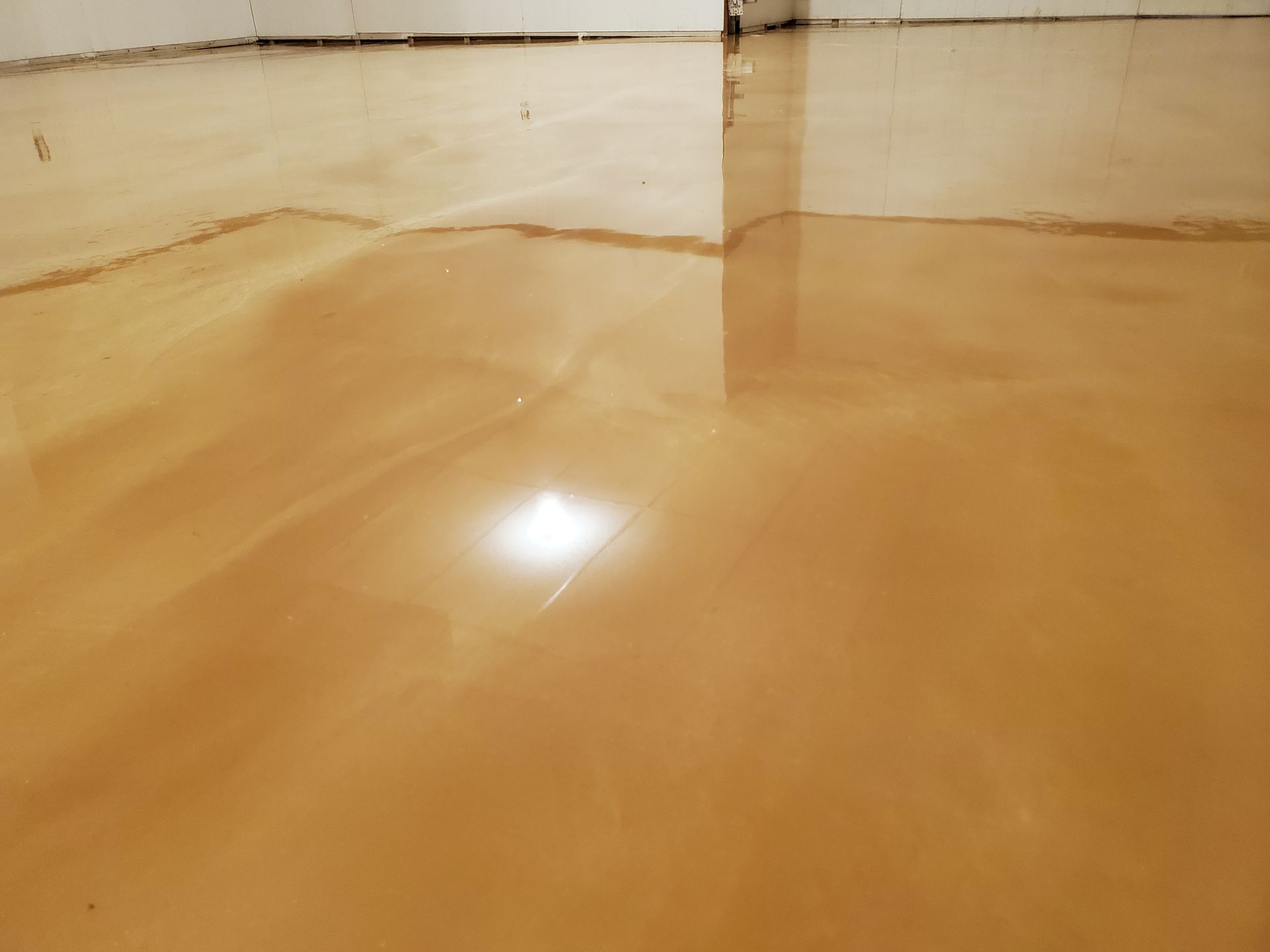 A glossy, light brown epoxy floor with a reflective surface and a visible seam in a room with white walls.