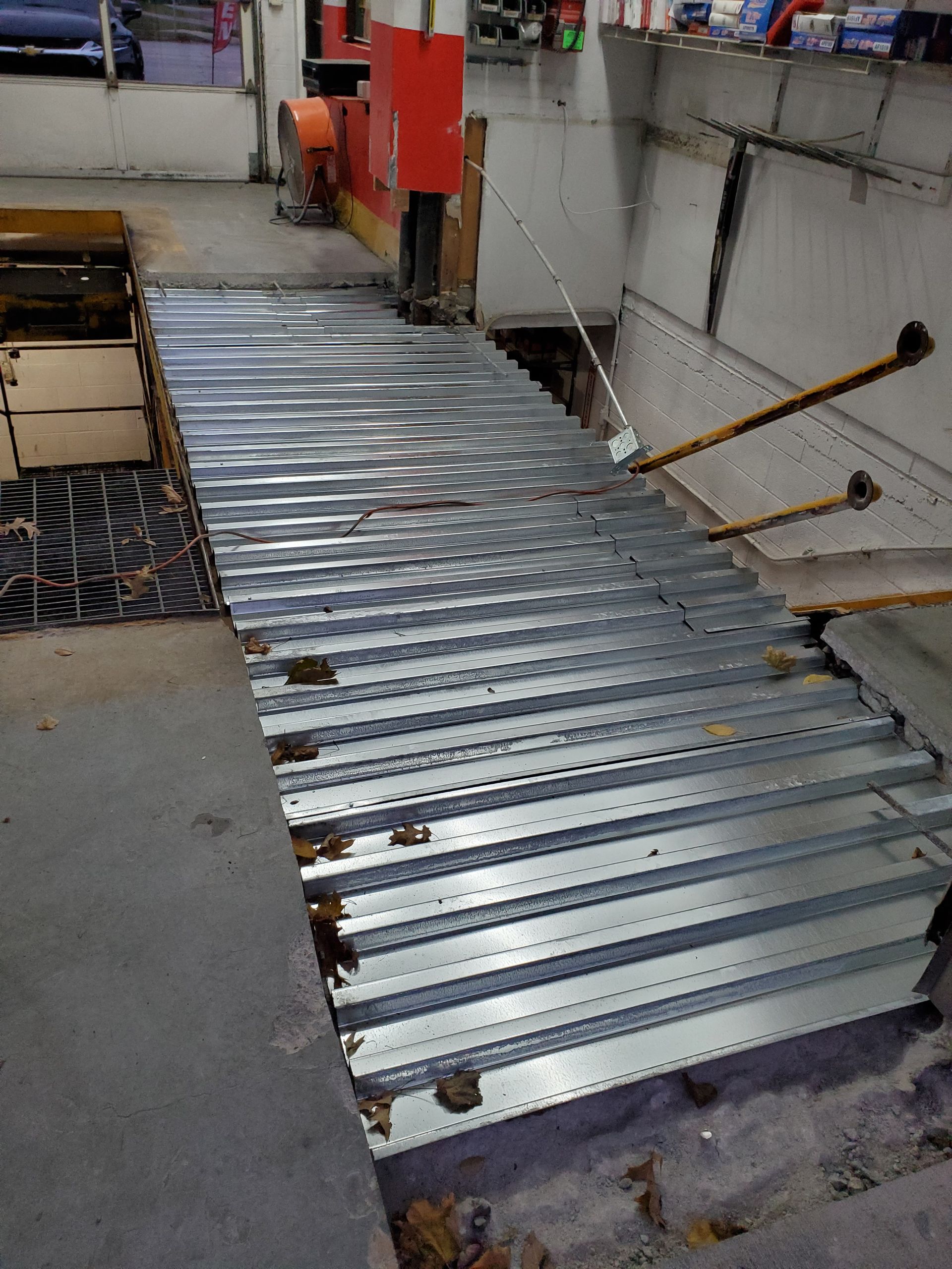 A metal staircase with perforated treads and yellow handrails under construction in a workshop area.