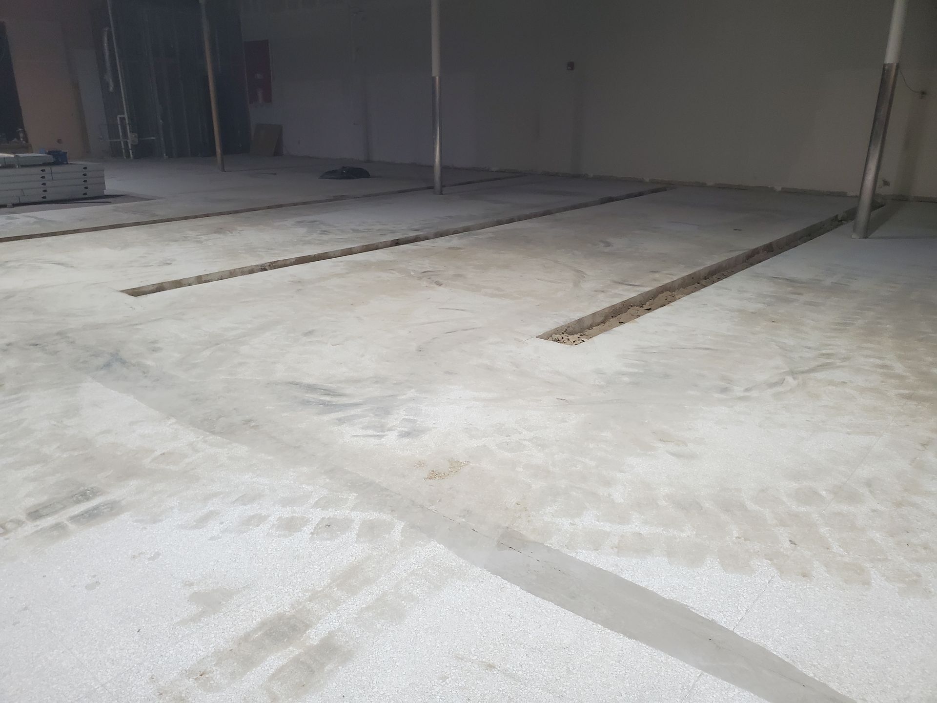 An indoor construction site features a concrete floor with two long, narrow trenches cut into the slab.