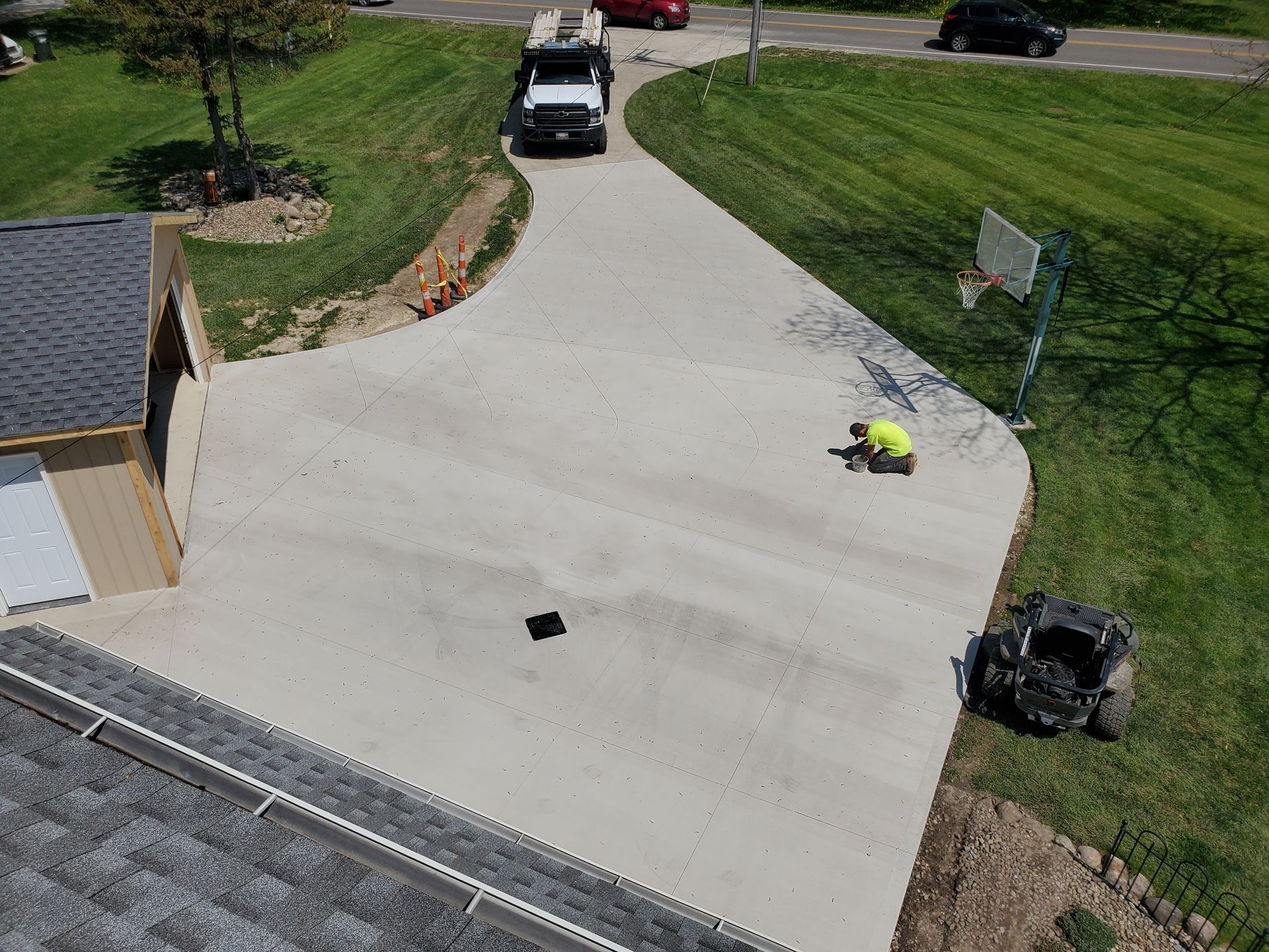An aerial view of a person in a neon shirt working on a newly poured concrete driveway next to a garage and house.