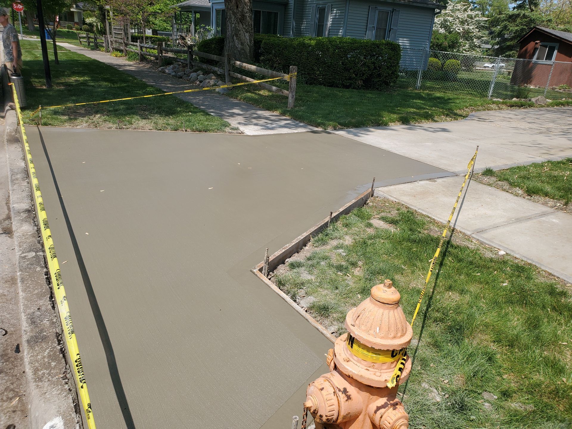 A newly poured concrete sidewalk section near a fire hydrant, cordoned off by yellow caution tape.