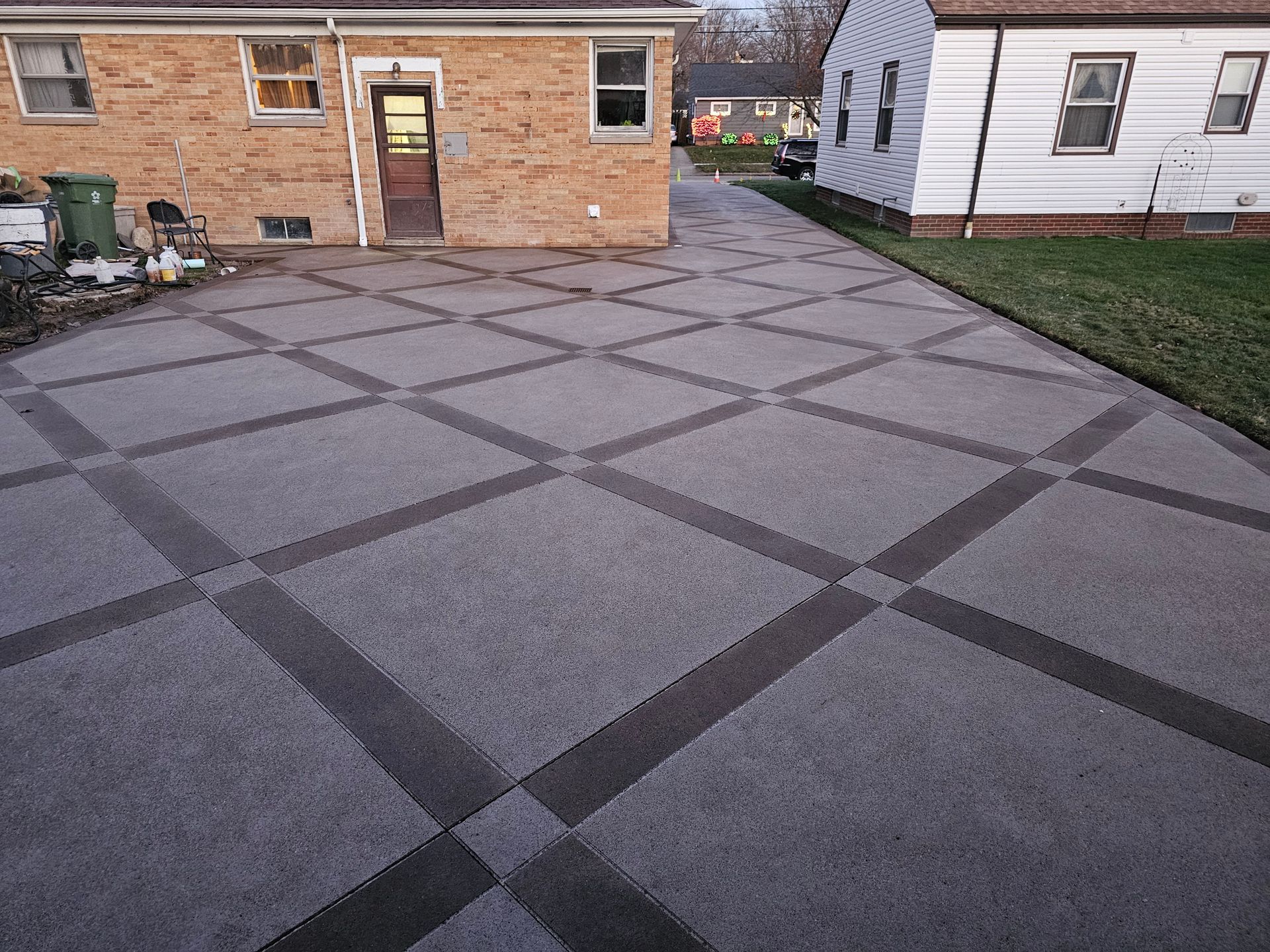 A driveway paved with grey concrete squares separated by a dark grid pattern, situated between two residential houses.