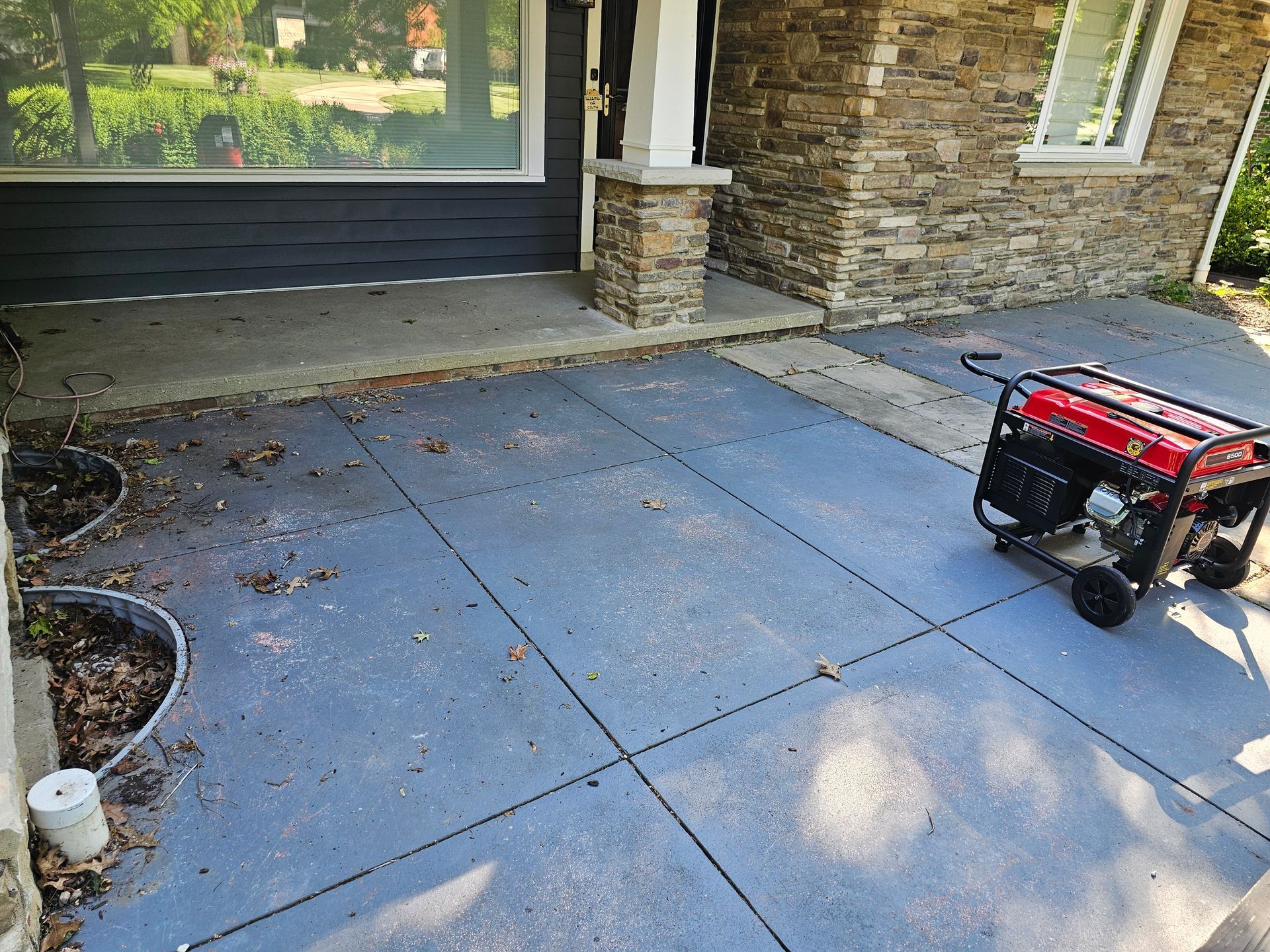 A red portable generator sits on a blue concrete patio outside a stone house porch.