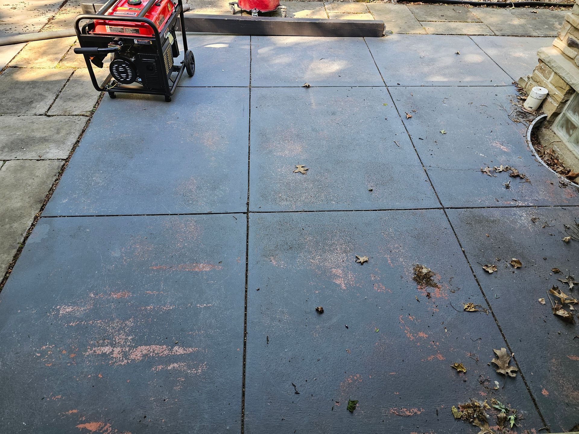 A portable red generator sits on a dark-grey patio made of large, square concrete pavers.