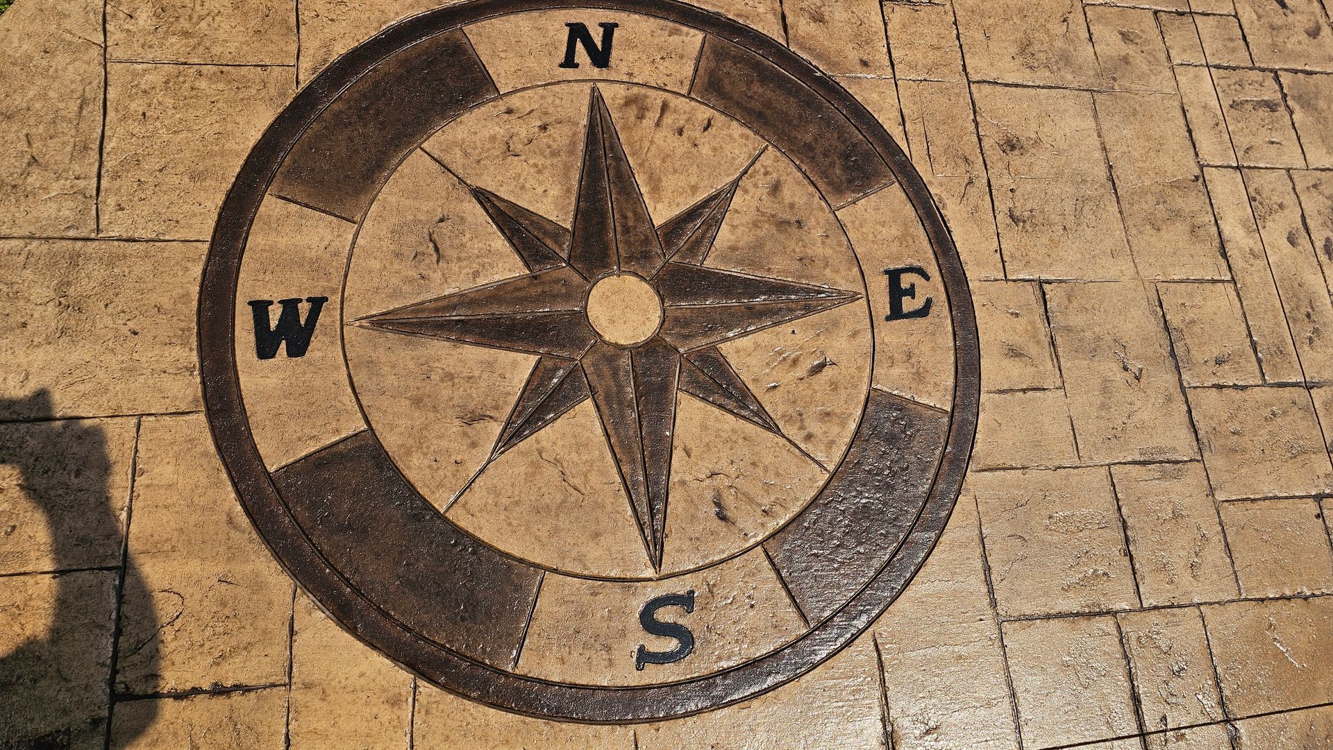 A compass rose design inlaid into light brown stone pavers with cardinal directions labeled N, E, S, and W.