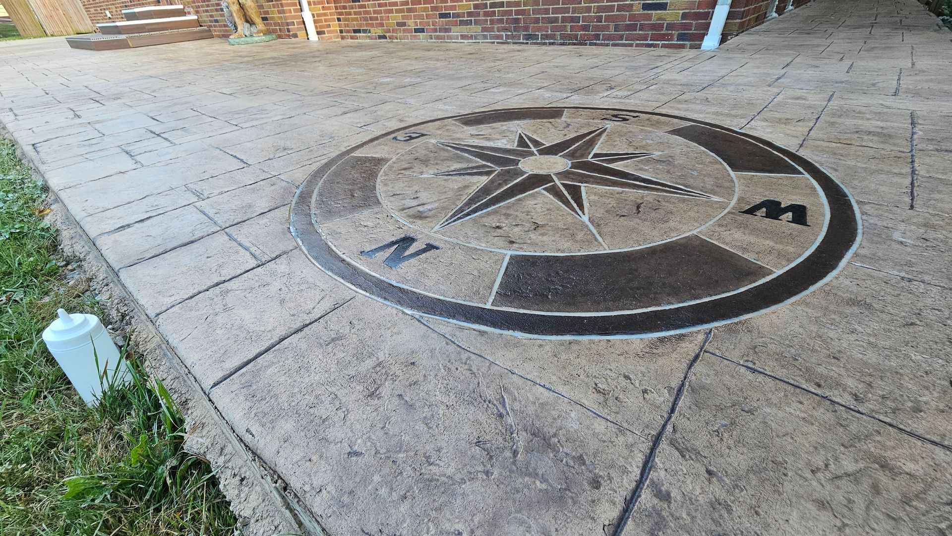 A beige, textured concrete patio featuring an embedded compass rose inlay design with dark brown accents.