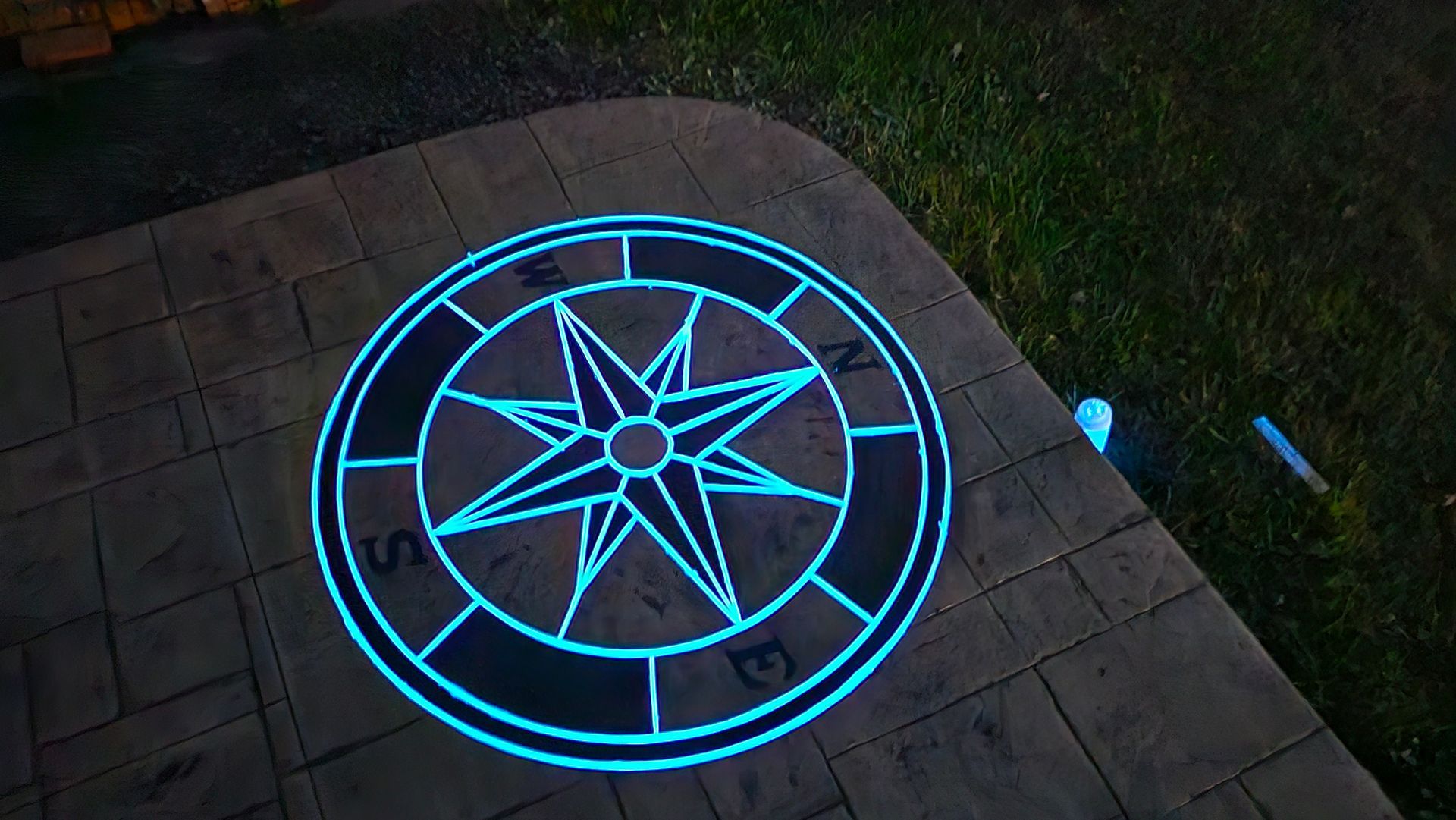 A glowing blue light projection of a compass rose on a stone patio at night.