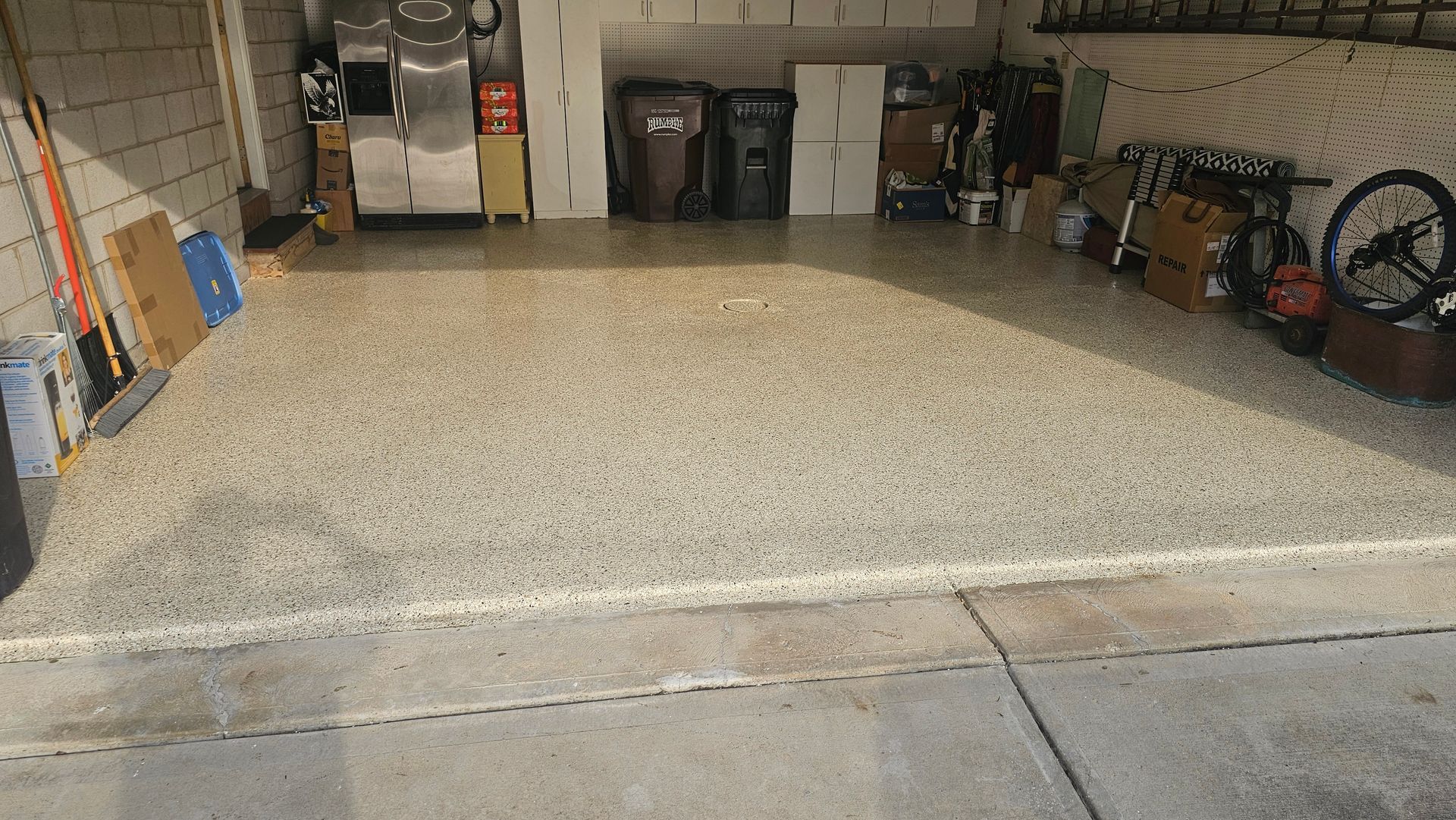A bright, clean garage with a speckled epoxy floor, storage bins, boxes, and a bicycle wheel leaning against the wall.
