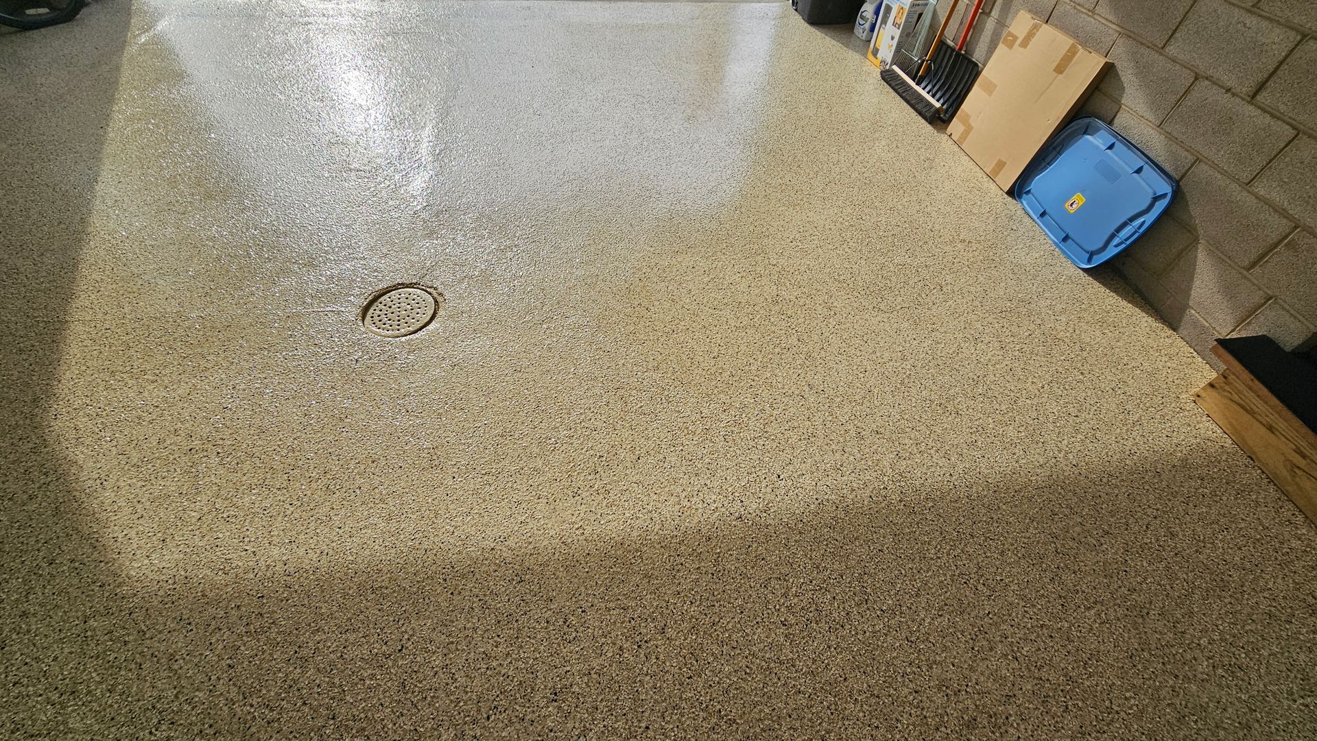 A freshly coated garage floor with a beige and brown speckled epoxy finish and a circular drain in the center.
