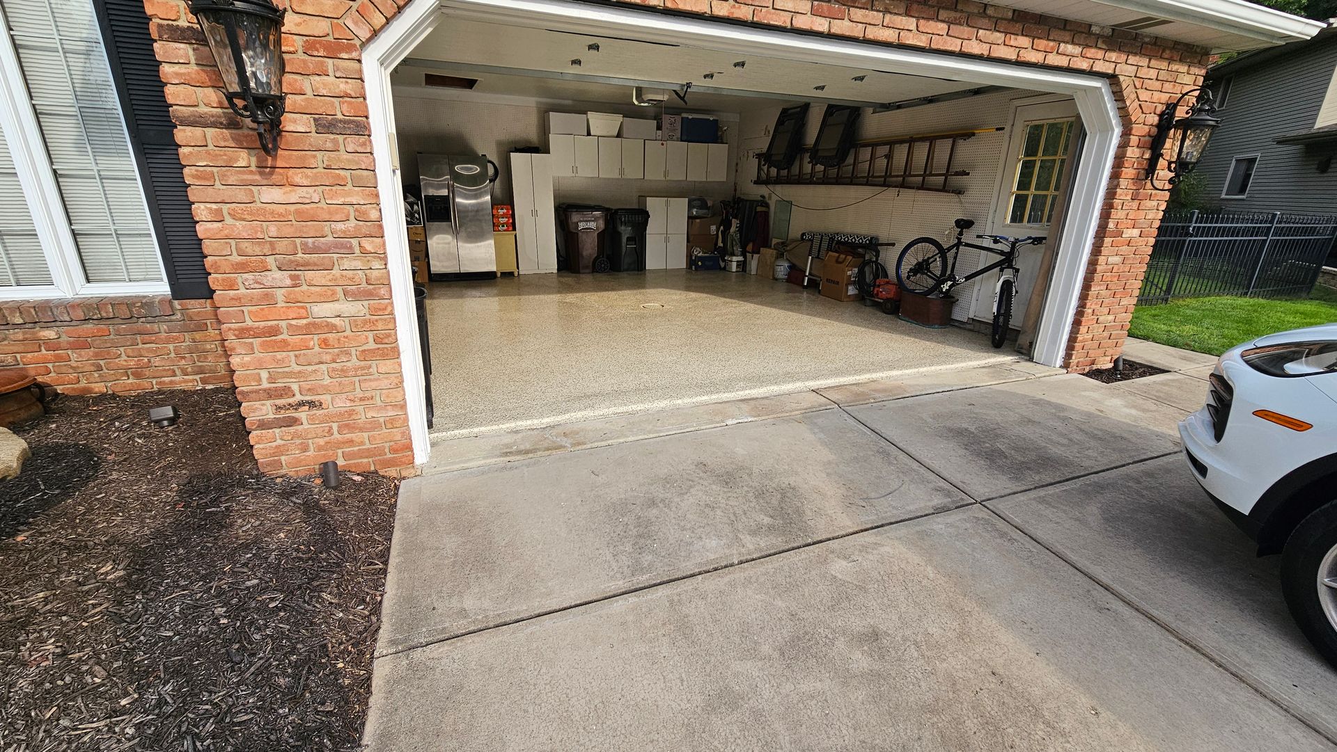 A brick garage with a clean, speckled floor, storage shelves, a bicycle, and a partial view of a white car on the driveway.