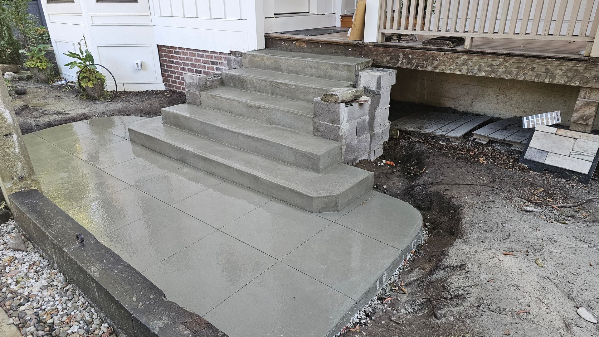 Newly poured concrete steps leading to a house porch, with an unfinished yard area surrounding the structure.