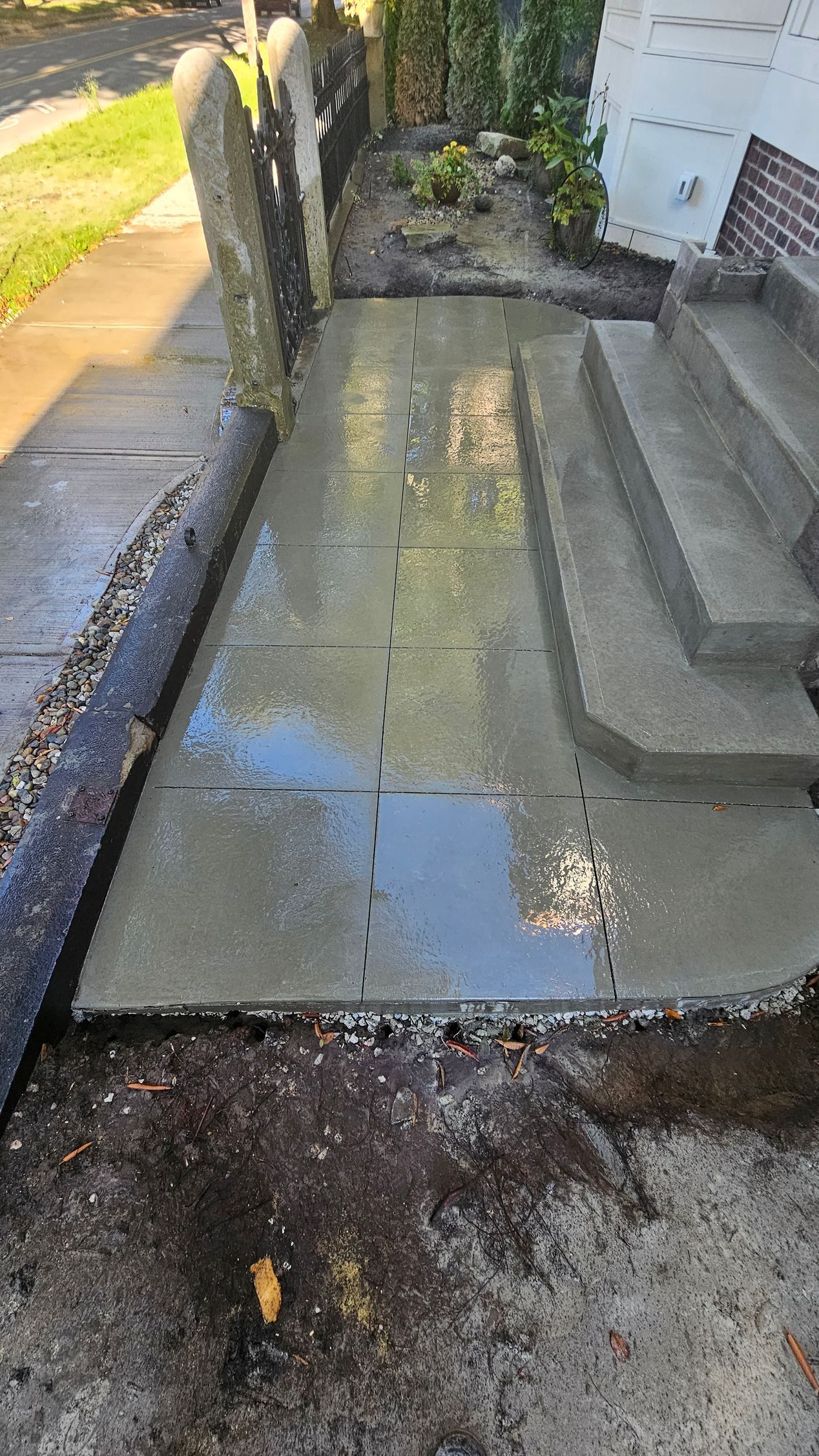 A newly poured concrete walkway with visible expansion joints leading to house steps, with standing water on the surface.