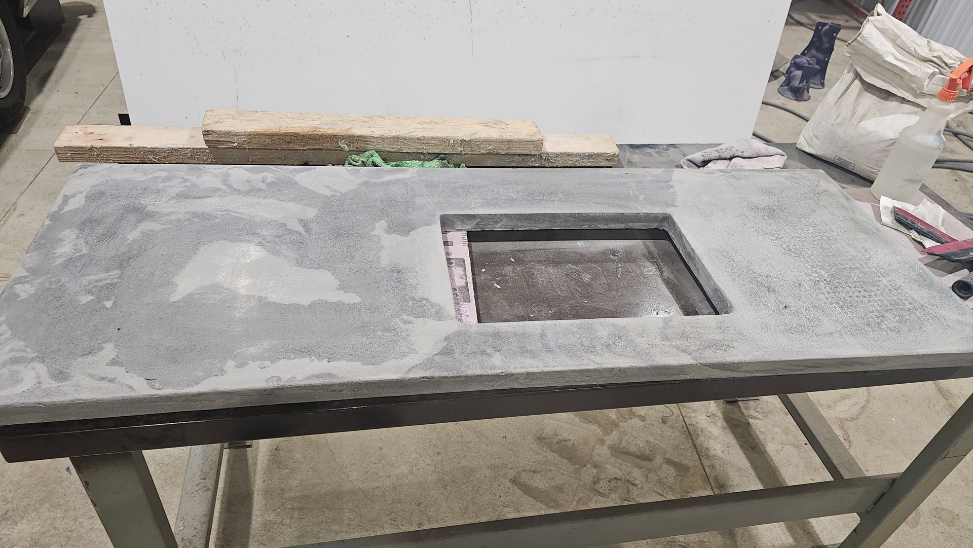 A gray rectangular concrete countertop with a rectangular cutout for a sink, resting on a metal work table.