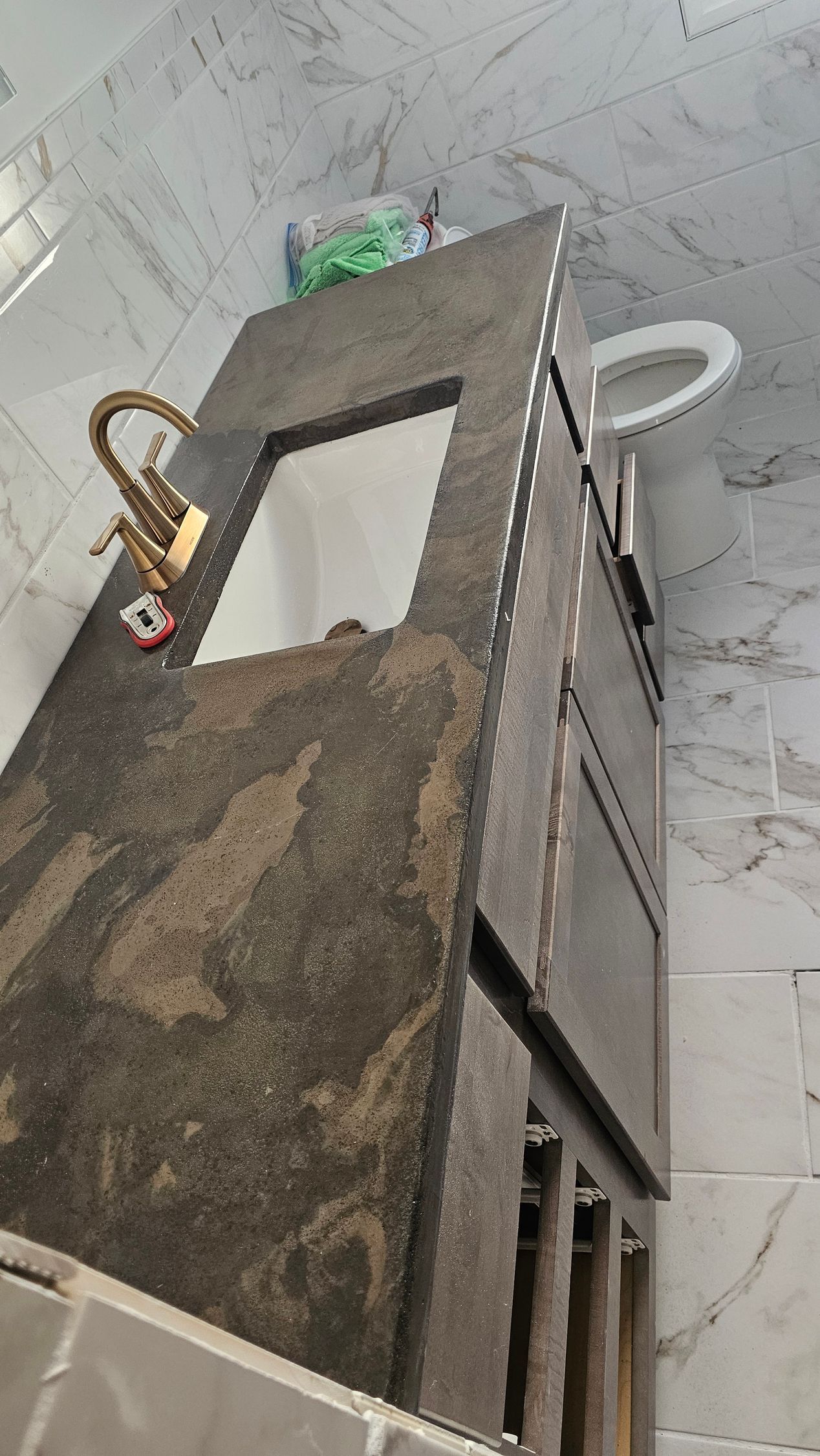 A vanity with a dark speckled stone countertop and gold faucet stands in a bathroom with white marble-patterned tiles.