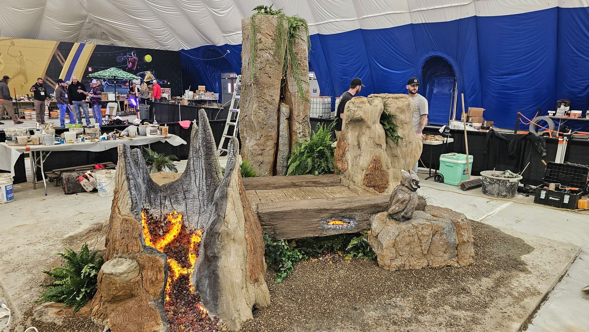 A large, foam-sculpted volcano display with glowing lava, surrounded by rocky platforms, inside a tented event space.