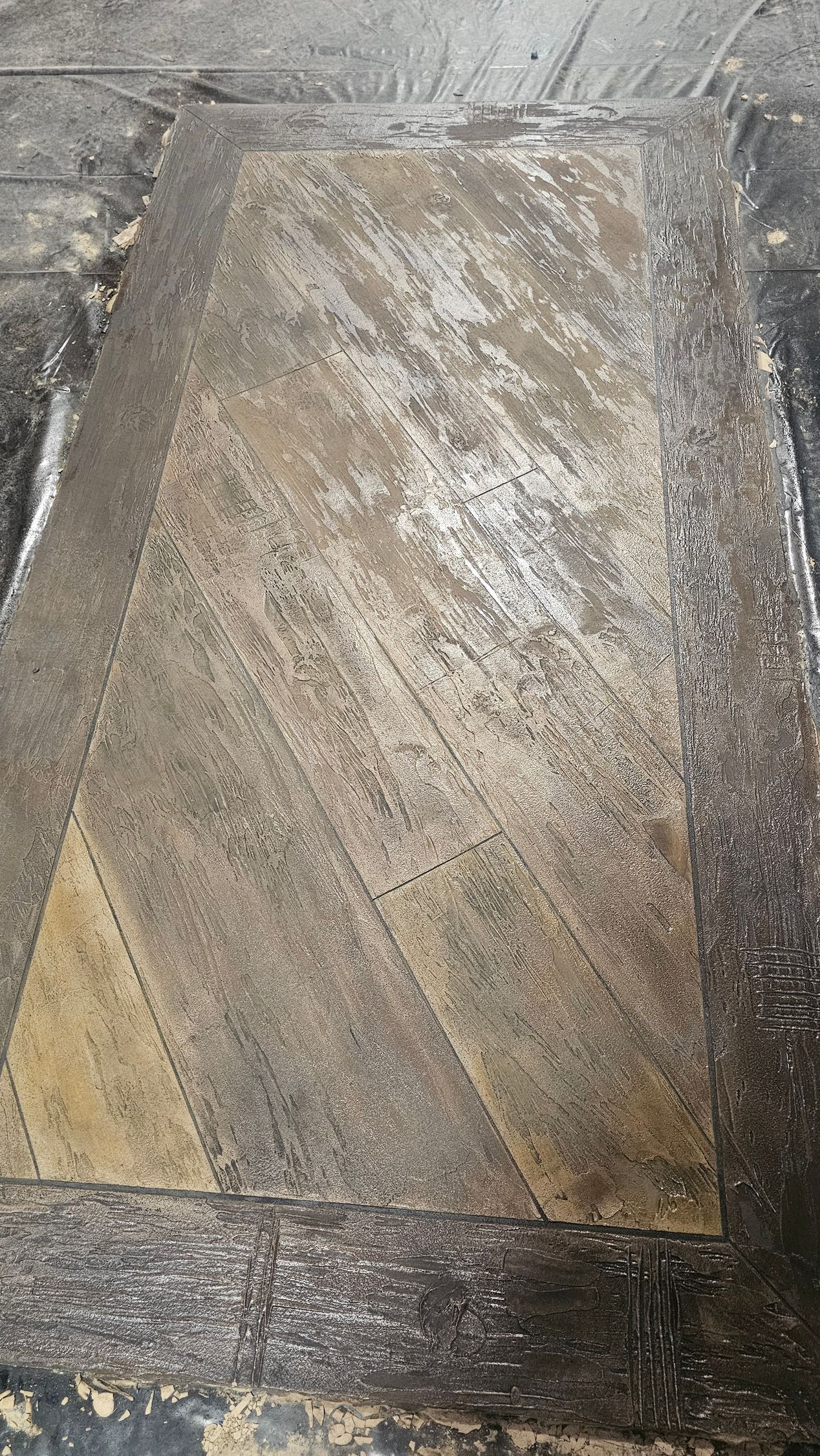 A rectangular stone paver with a textured, mottled beige and grey surface, framed by a border of dark, jagged stone debris.
