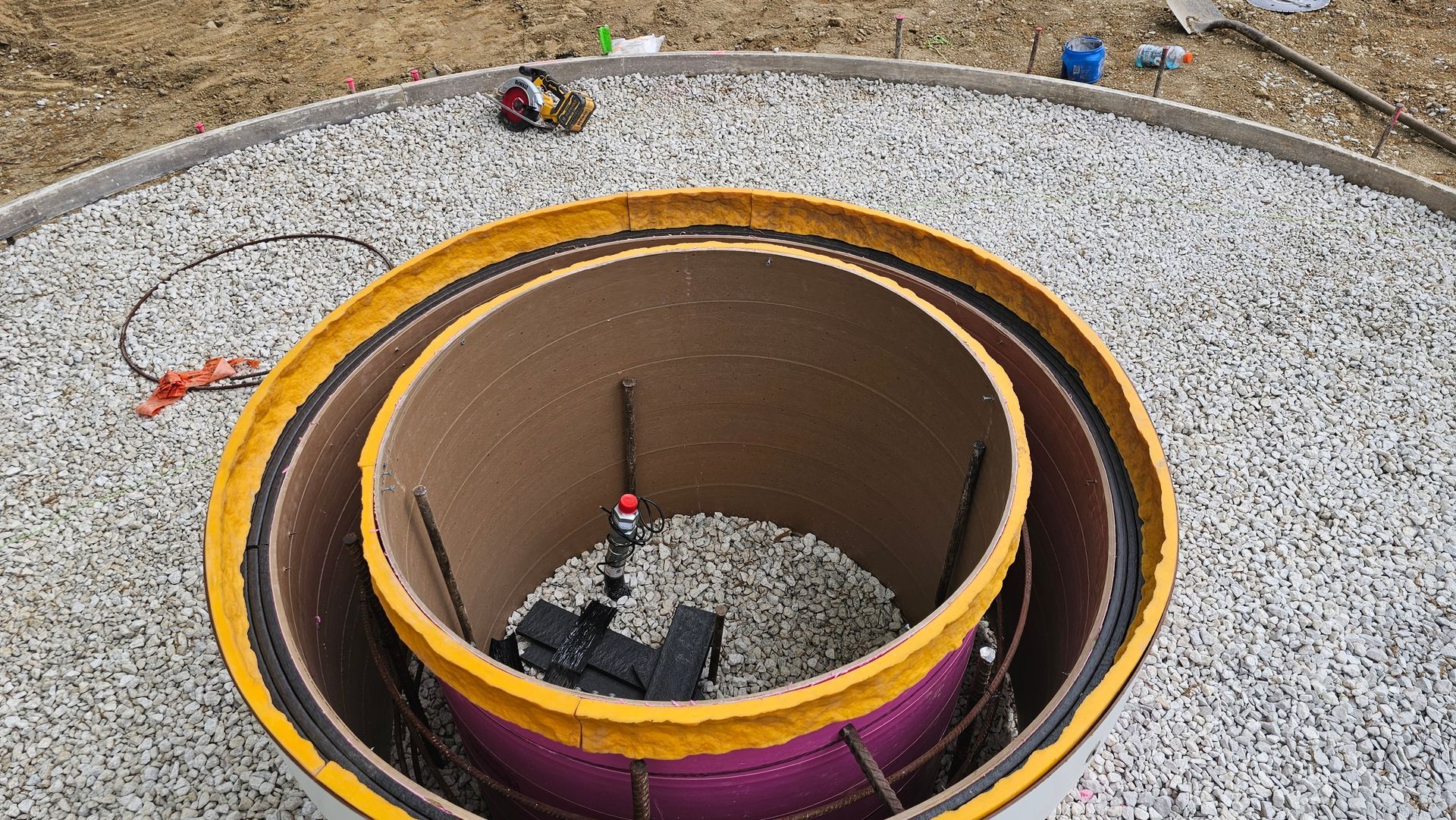 A round construction formwork setup with an inner cardboard tube and steel reinforcement sitting on a gravel bed.