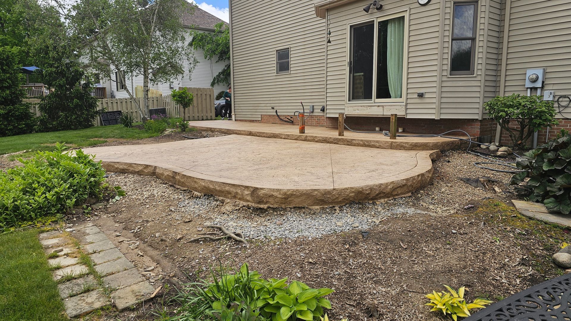 An unfinished patio area with beige gravel surrounded by a curved timber border, situated in a backyard.