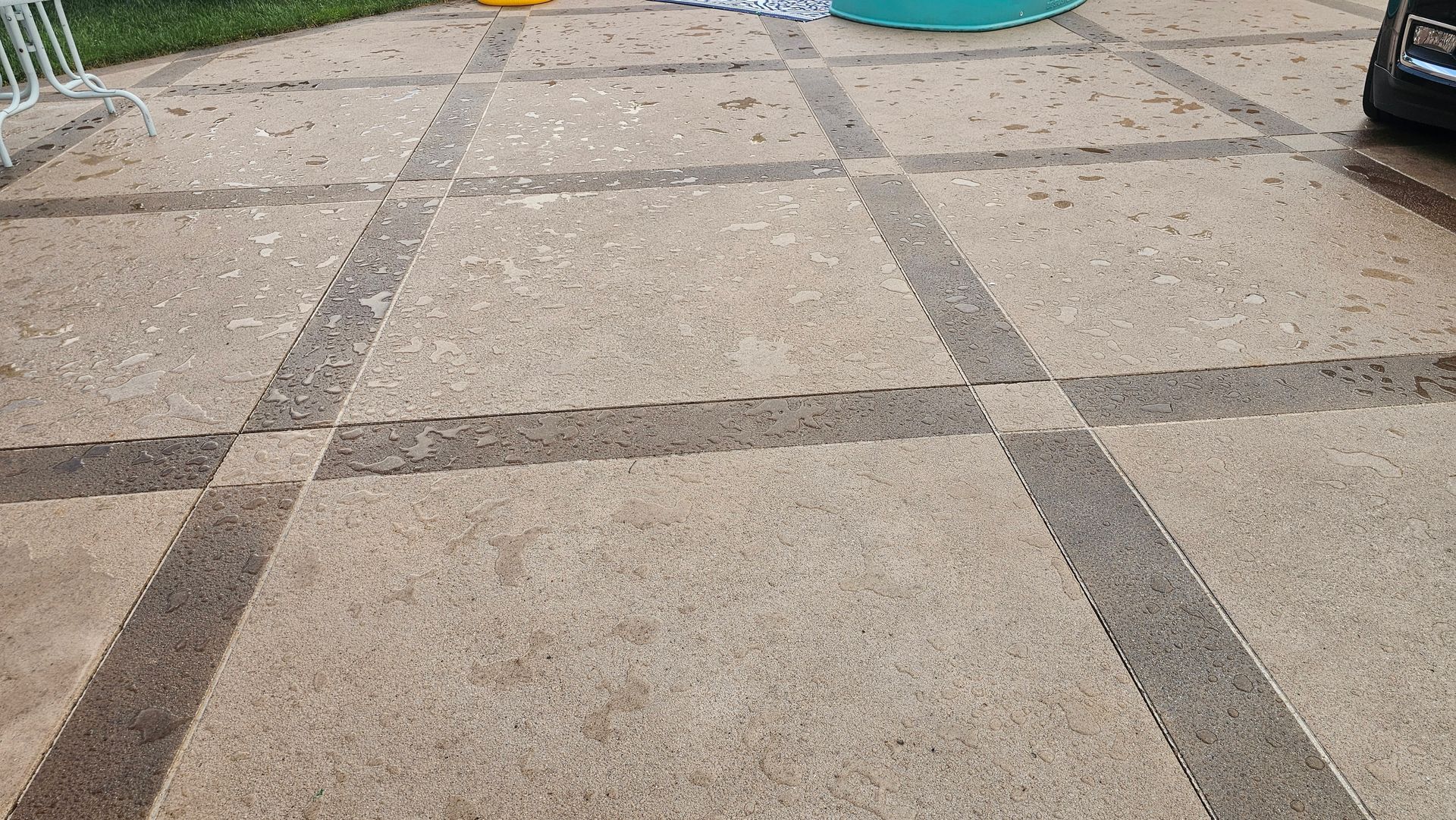 A concrete patio featuring a grid pattern of smooth light-colored squares bordered by darker, textured strips.