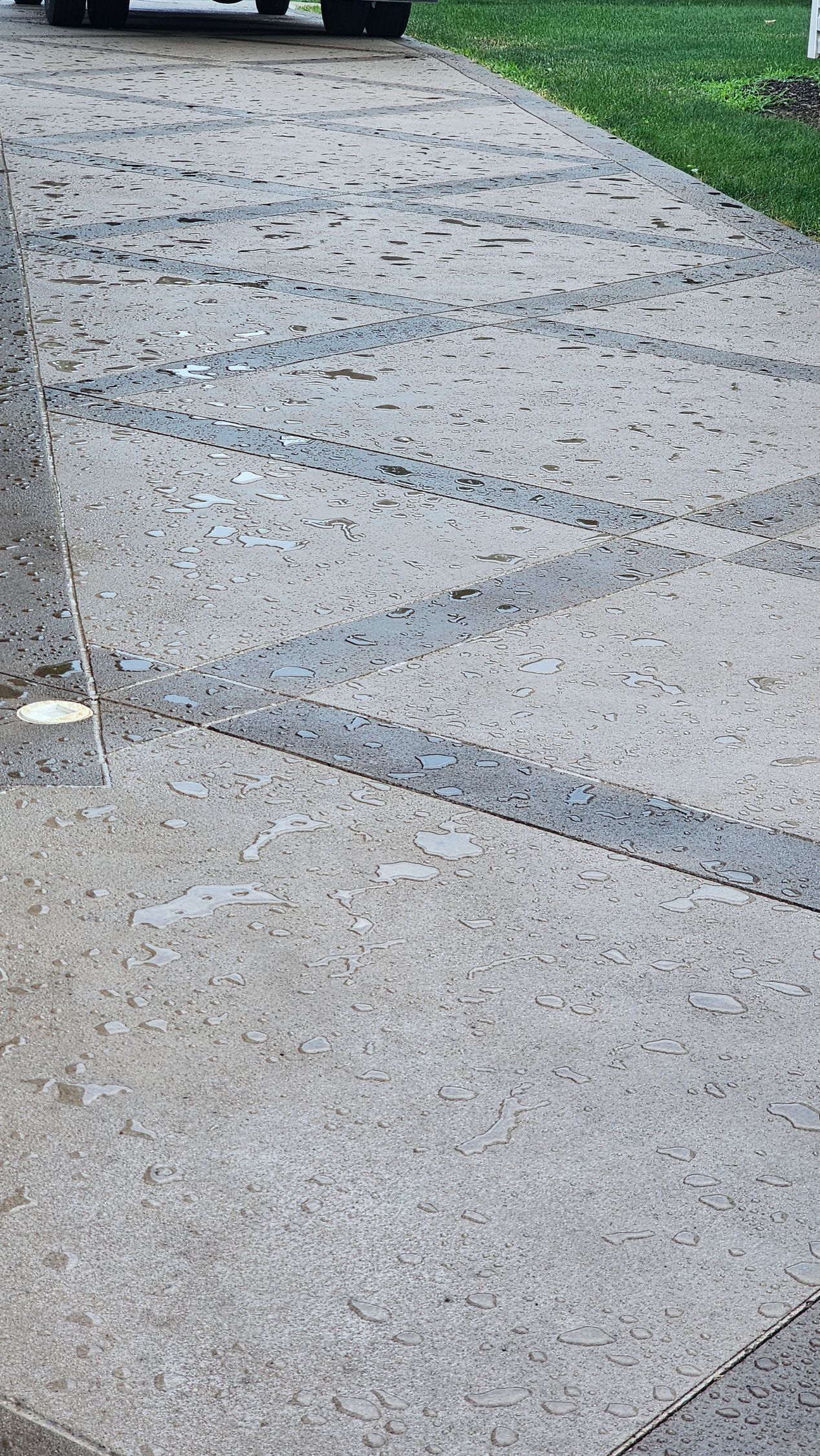A light-colored concrete driveway featuring a decorative pattern of dark, gravel-filled diagonal grooves.