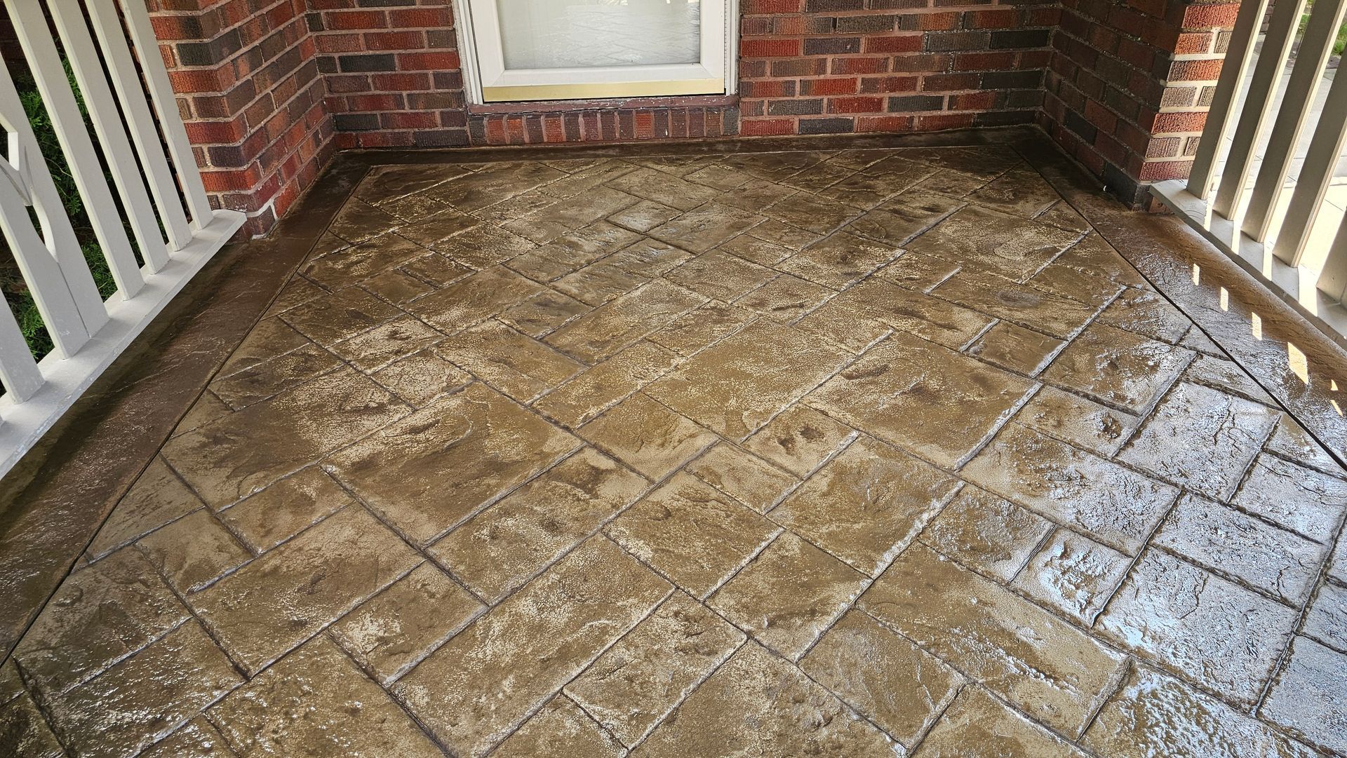 A stone-patterned porch floor with a mix of brown and grey tones, framed by a brick wall and white porch railings.