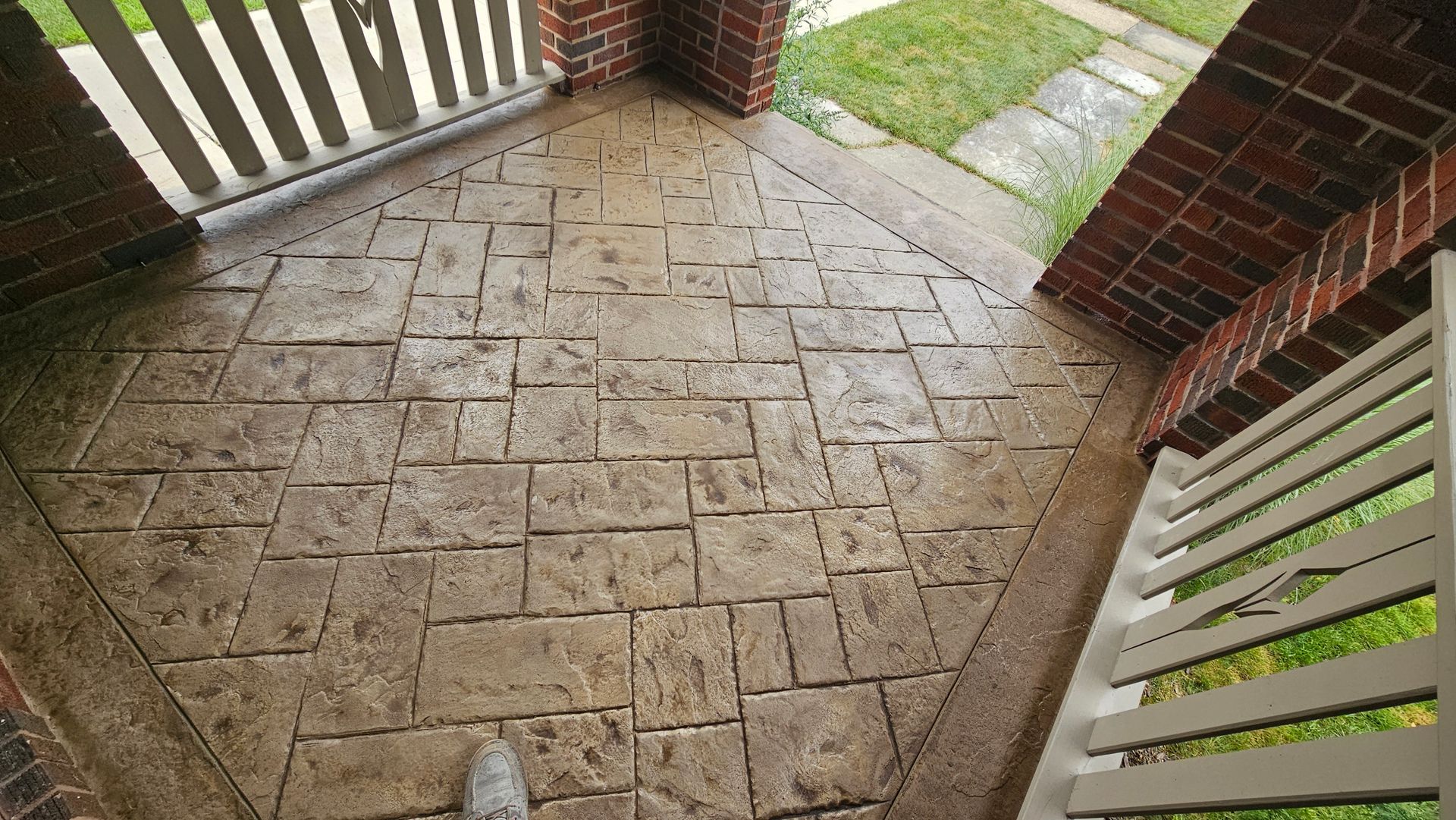 A stamped concrete porch with a tan, block-pattern design framed by brick columns and white railings.