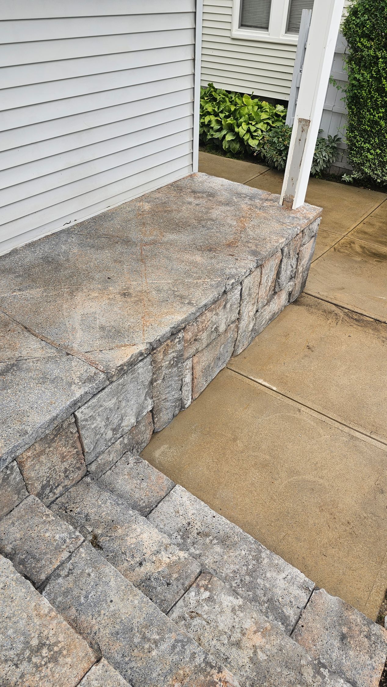 Stone steps and a raised stone landing platform leading up to the side of a white-sided house.
