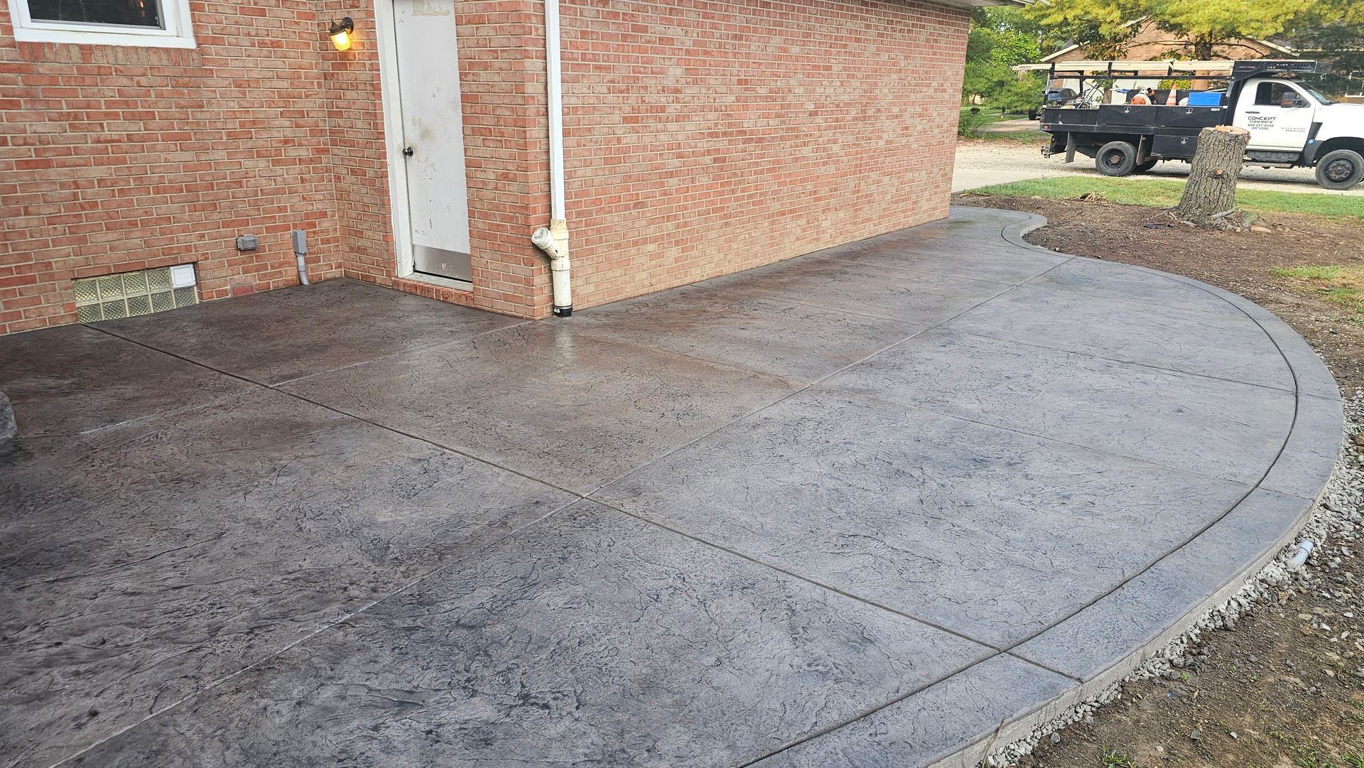 A gray stamped concrete patio with a curved edge attached to the side of a brick house.