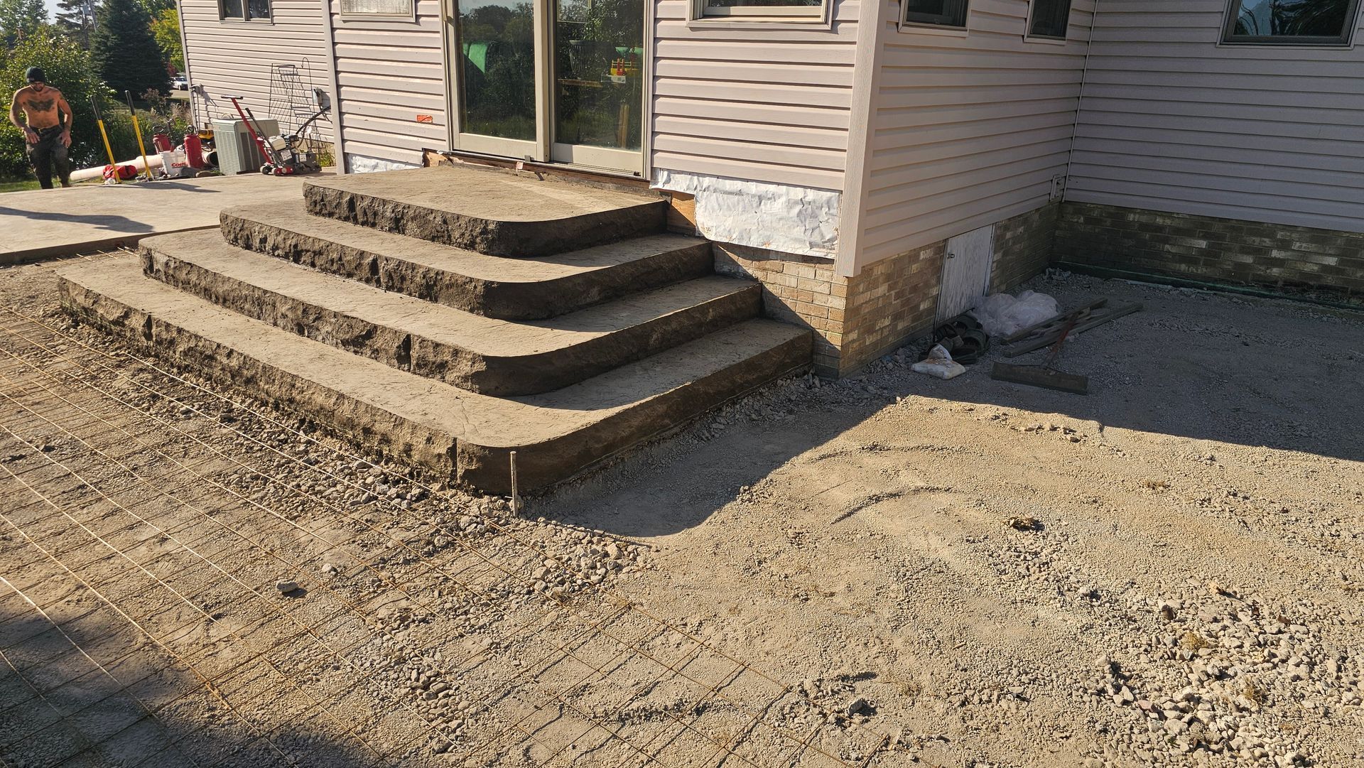 Stone steps leading to a house entrance under construction with a gravel yard and unfinished siding.