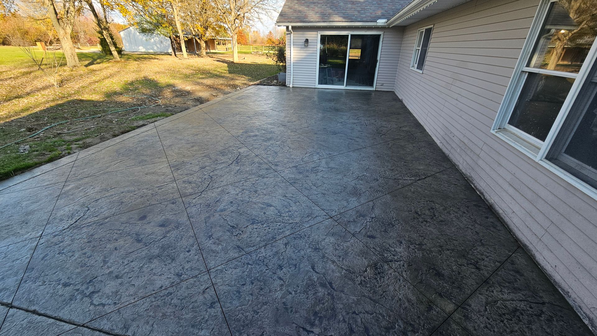 A stamped concrete patio featuring a gray textured pattern outside a house with a glass sliding door and light siding.
