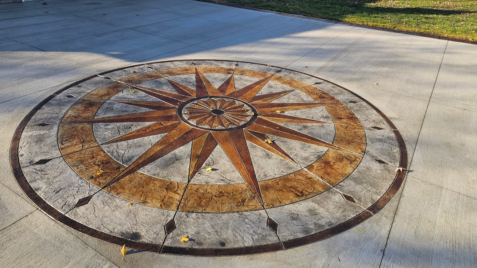 A compass rose mosaic in brown and gray tones, inlaid in a concrete outdoor patio.