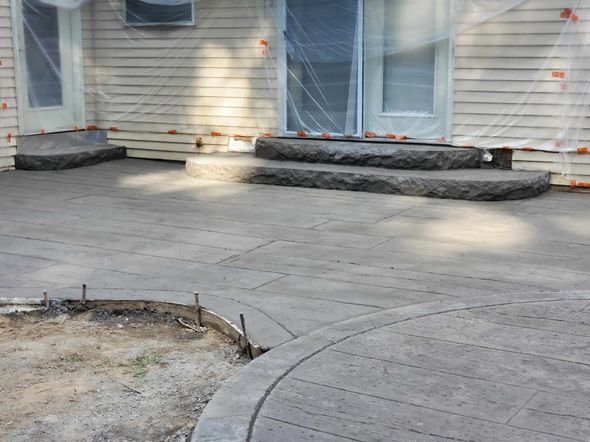 Newly installed concrete patio and steps leading to a house with beige siding, showing construction in progress.