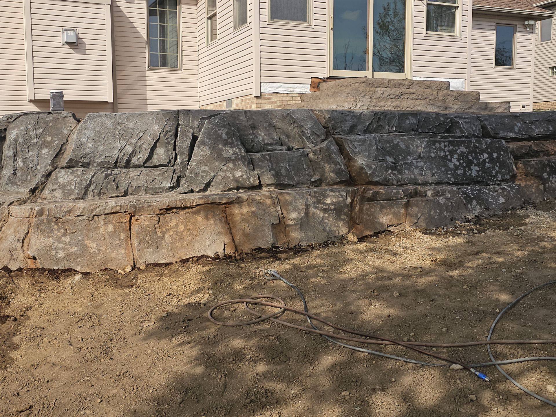 A stone retaining wall built into a slope in front of a house with light-colored siding.